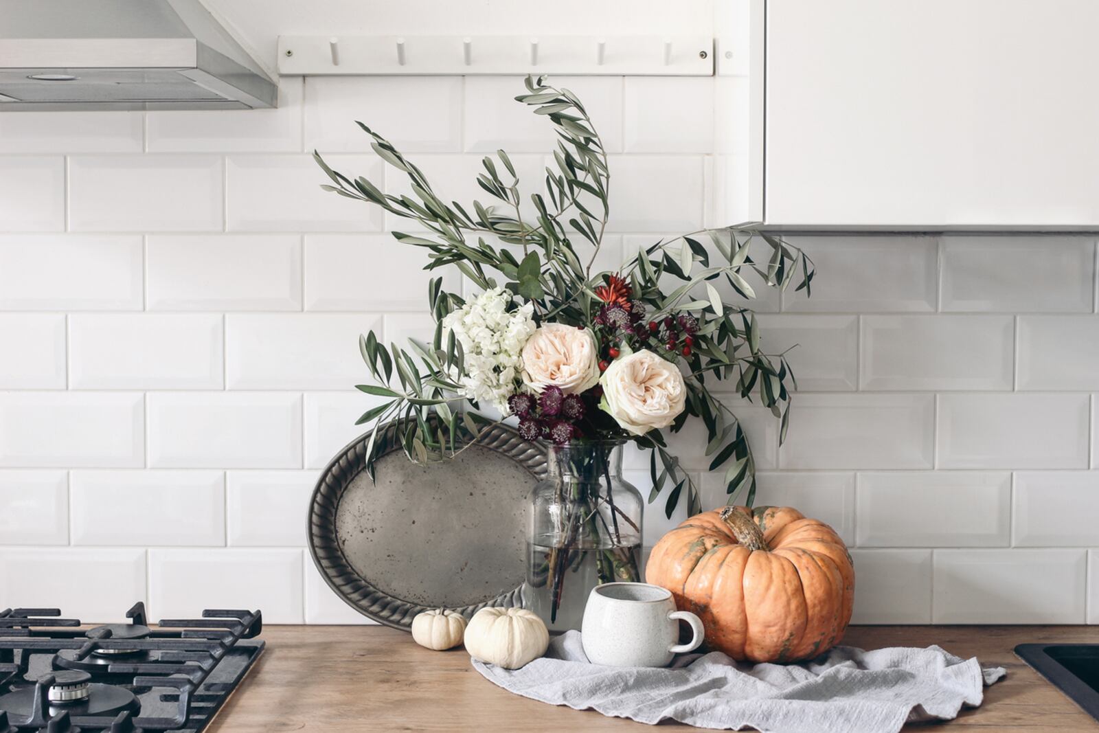 This autumn still life composition in a rustic eclectic kitchen interior includes a cup of coffee, vintage silver tray and floral bouquet. Bring artisanal pieces into your fall décor by using textured artisanal trays, created with terracotta, plaster, or copper, vintage brass candlesticks or handmade pieces. iSTOCK/COX