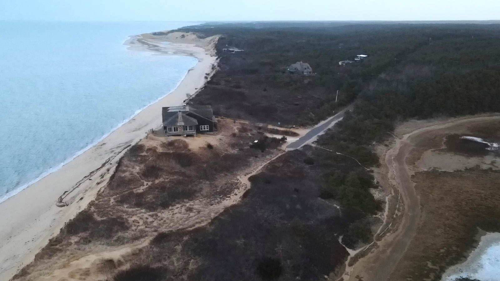 A home, center left, sits atop of a sandy bluff overlooking a beach in Wellfleet, Mass., Wednesday, Jan. 29, 2025. (AP Photo/Andre Muggiati)