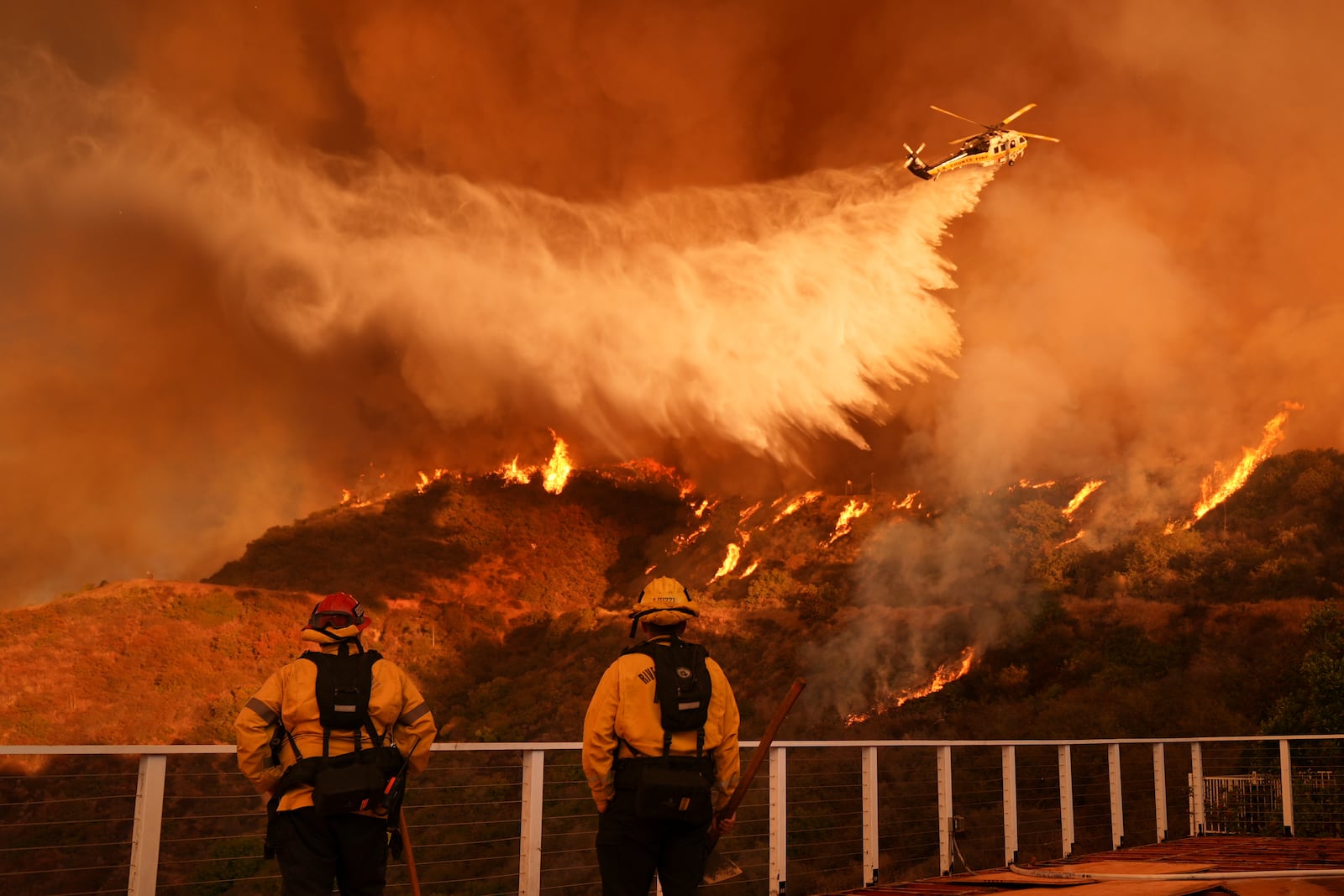 Firefighters watch as water is dropped on the Palisades Fire in Mandeville Canyon Saturday, Jan. 11, 2025, in Los Angeles. (AP Photo/Jae C. Hong)