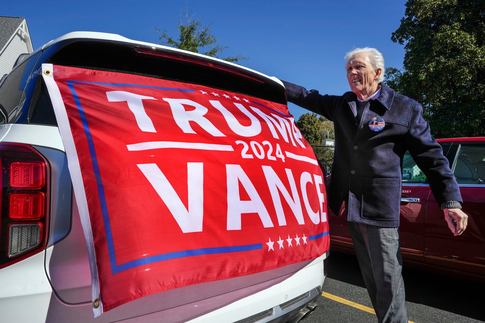 Douglas MacDonald, of Rutherfordton, attaches a flag to the back of his car at the Rutherford County Annex Building where early voting was taking place, Thursday, Oct. 17, 2024 in Rutherfordton, N.C. (AP Photo/Kathy Kmonicek)