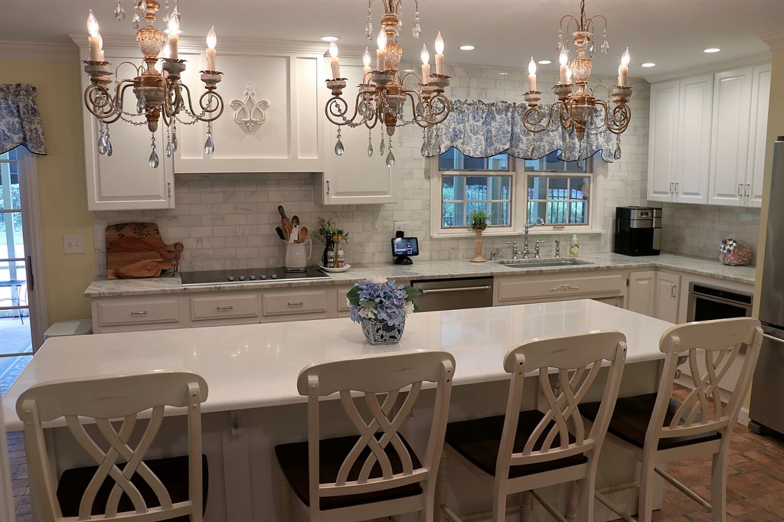 Crystal chandeliers hang above the long narrow island in the kitchen. The island has a Corian counter that extends to allow bar seating.