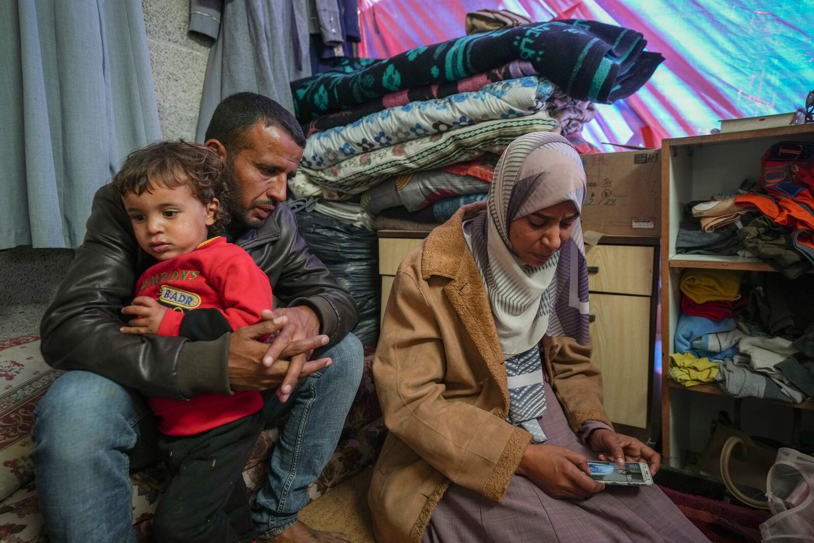 Areej al Qadi, right, shows a picture of one of her three dead children as her husband Mahmoud bin Hassan, left, holds a fourth surviving child at their tent in a refugee camp in Deir al-Balah, Gaza Strip, Thursday Nov. 21, 2024. Seven-year-old Hamza, his five-year-old brother Abdelaziz, and his four-year-old sister Laila Hassan were among 9 people killed by an Israeli strike in Khan Younis on Wednesday. Palestinian health officials say the death toll in the Gaza Strip from the 13-month-old war between Israel and Hamas has surpassed 44,000. (AP Photo/Abdel Kareem Hana)