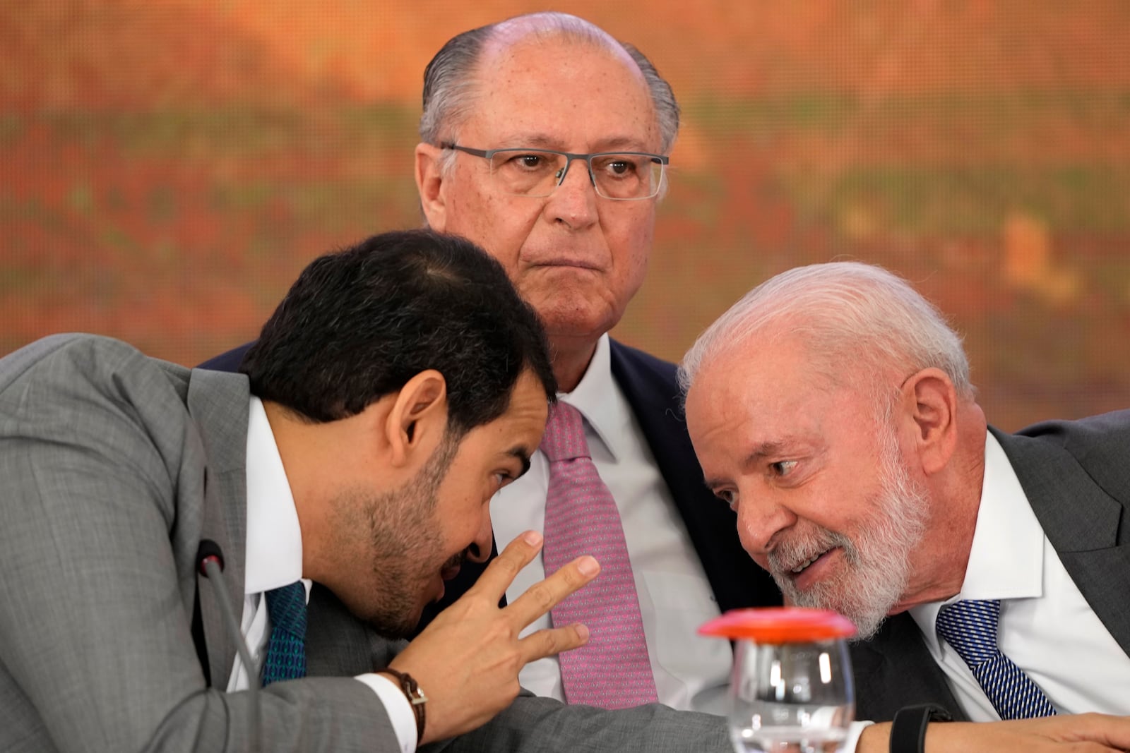 Brazil's Attorney General Jorge Messias, left, leans over to speak with President Luiz Inacio Lula da Silva at a signing ceremony of a compensation agreement for damages caused by the 2015 collapse of the Mariana dam owned by the mining company Samarco, a joint venture of Vale and BHP, at the Planalto Presidential Palace, in Brasilia, Brazil, Friday, Oct. 25, 2024. Pictured center is Vice President Geraldo Alckmin. (AP Photo/Eraldo Peres)