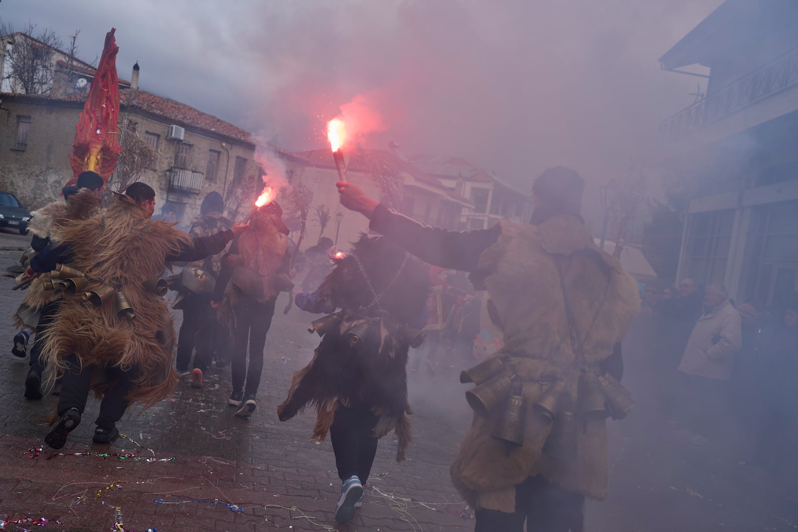 Revellers dressed in animal skins and heavy bronze bells, hold up flares during carnival celebrations in Distomo, a village in central Greece, on Monday, March 3, 2025. (AP Photo/Petros Giannakouris)