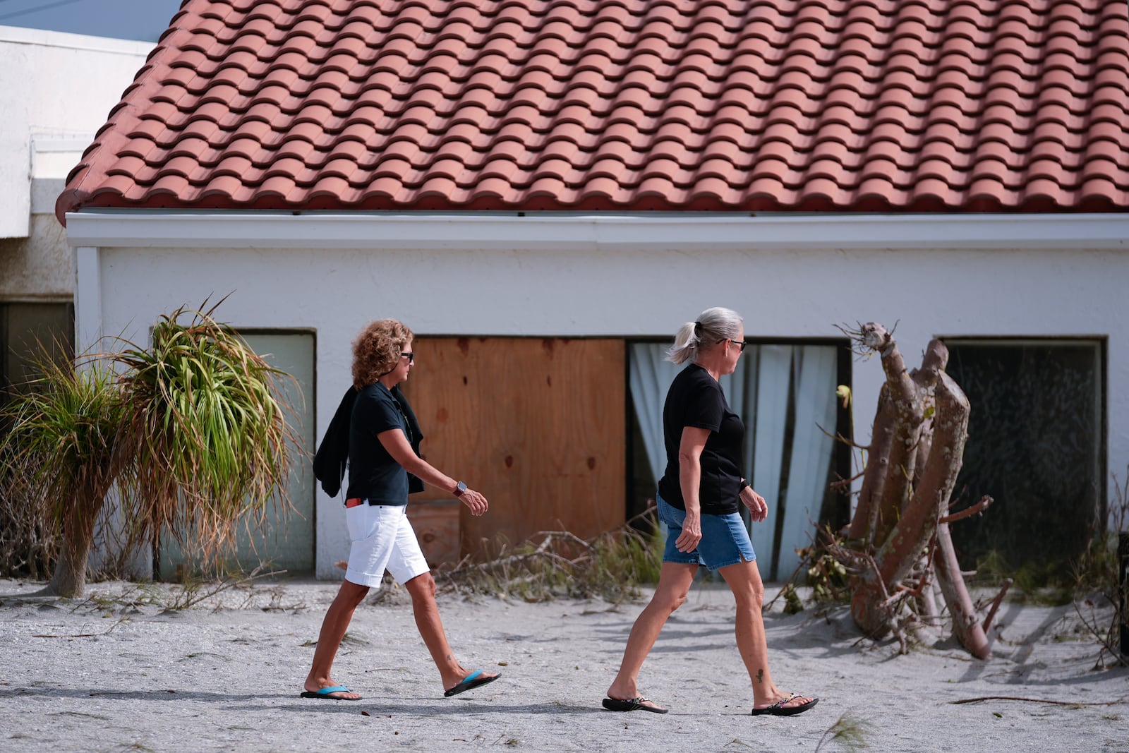 Area residents walk past a beachfront home with sand reaches half-way up its sliding doors, as they survey Hurricane Milton damage, on the island of Venice, Fla., Friday, Oct. 11, 2024. (AP Photo/Rebecca Blackwell)