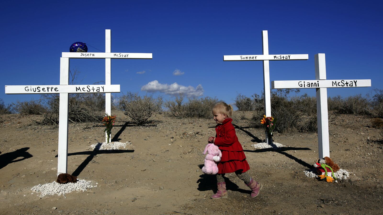 The young daughter of a family friend plays with a stuffed toy left at the memorial for Joseph McStay, 40, Summer McStay, 43, Gianni McStay, 4, and Joseph McStay Jr., 3, near the spot in the Mojave Desert where the family's remains were found buried in a shallow grave in November 2013. The family had been missing since February 2010.