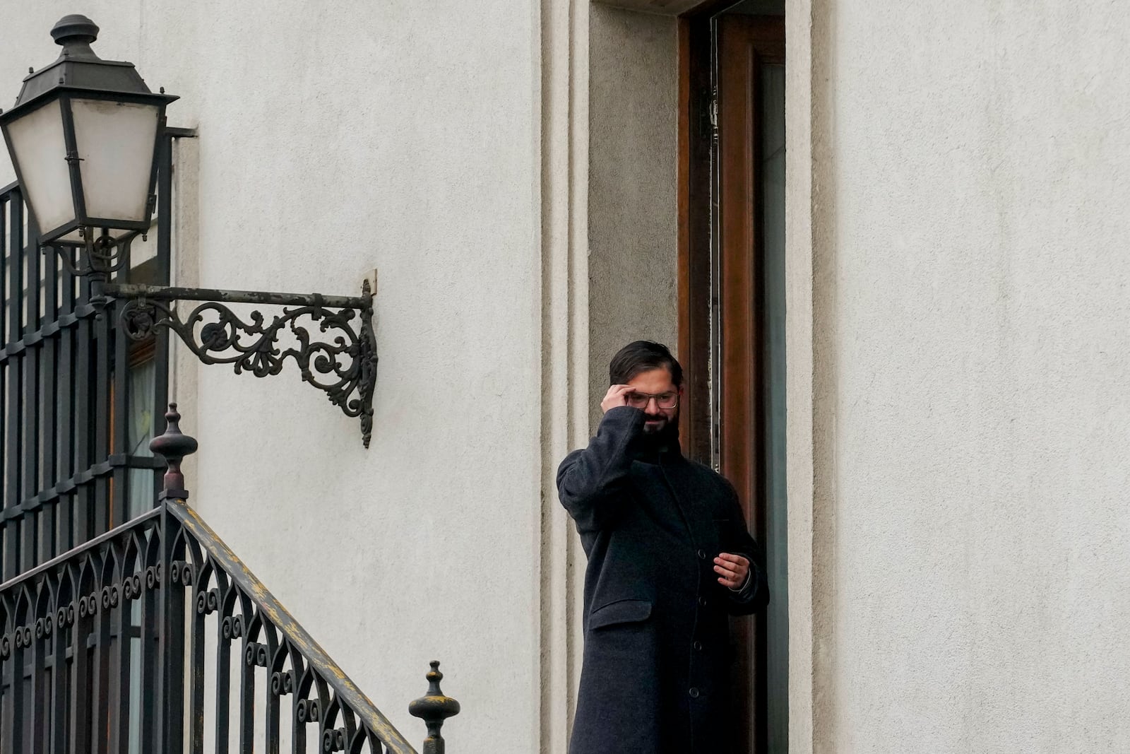 FILE - President Gabriel Boric adjusts his glasses while standing outside his office at La Moneda presidential palace, in Santiago Chile, May 29, 2024. (AP Photo/Esteban Felix, File)