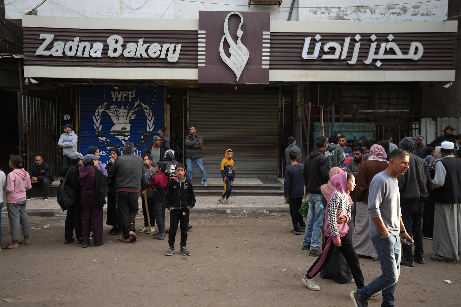 Palestinians gather near a closed bakery amid a shortage in flour and the closure of a main bakery in central Gaza have exacerbated an already dire humanitarian situation, in Deir al-Balah, Gaza Strip, Monday, Nov. 18, 2024. (AP Photo/Abdel Kareem Hana)