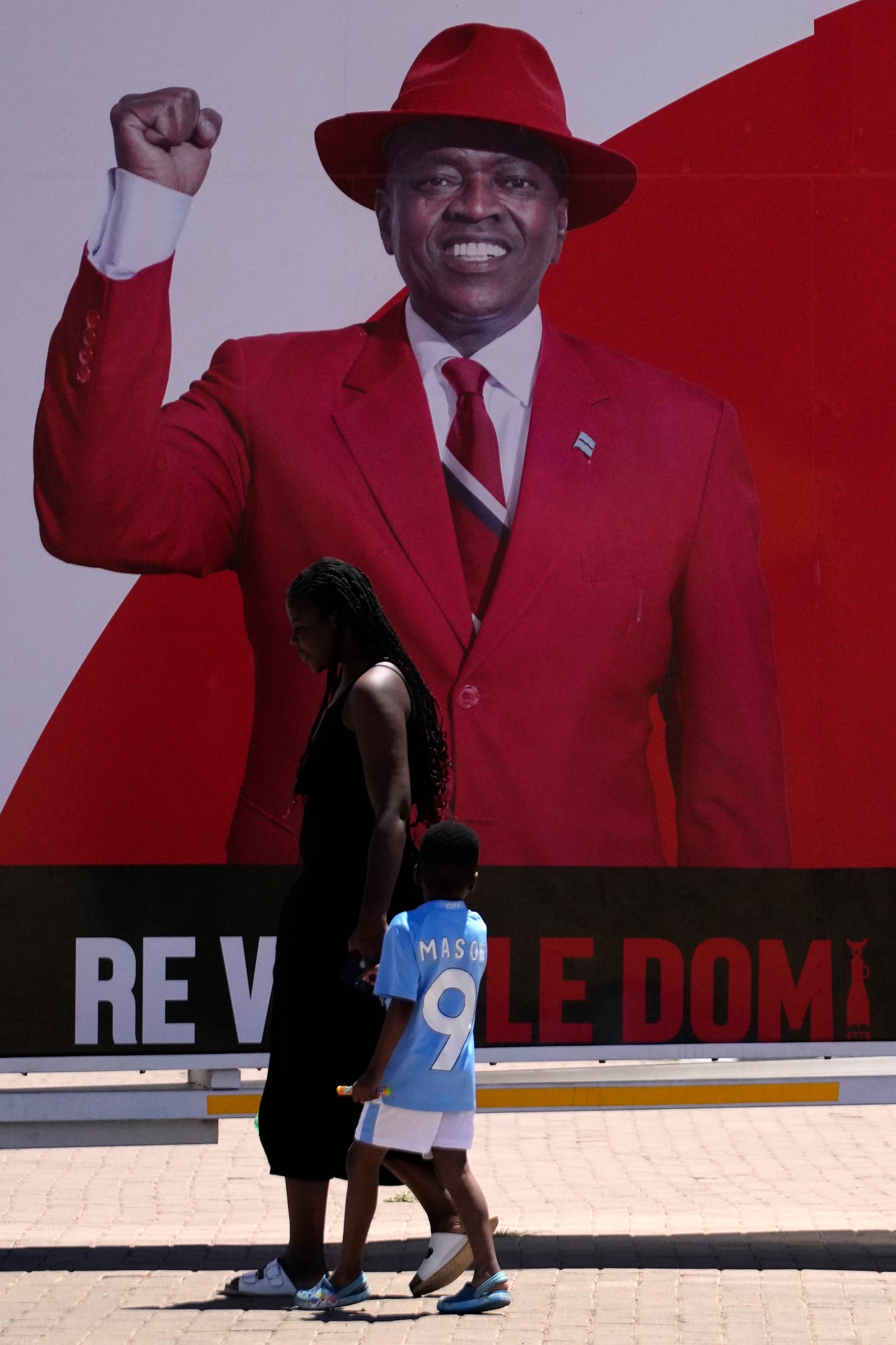 A woman and a child passes an election poster of ruling party Botswana Democratic Party president Mokgweetsi Masisi in Gaborone, Botswana, Tuesday, Oct. 29, 2024. (AP Photo/Themba Hadebe)