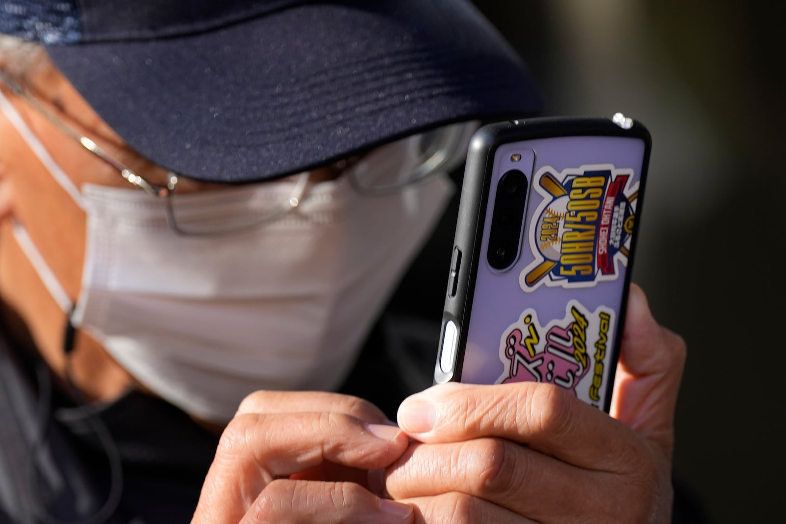 A man uses a mobile phone with a decoration to celebrate an achievement of Shohei Ohtani of the Los Angeles Dodgers as he and others gather to watch a live stream of Game 3 of the baseball World Series between the Dodgers and the New York Yankees during a public viewing event in Oshu, northeastern Japan, the hometown of Shohei Ohtani of the Los Angeles Dodgers, Tuesday, Oct. 29, 2024. (AP Photo/Eugene Hoshiko)