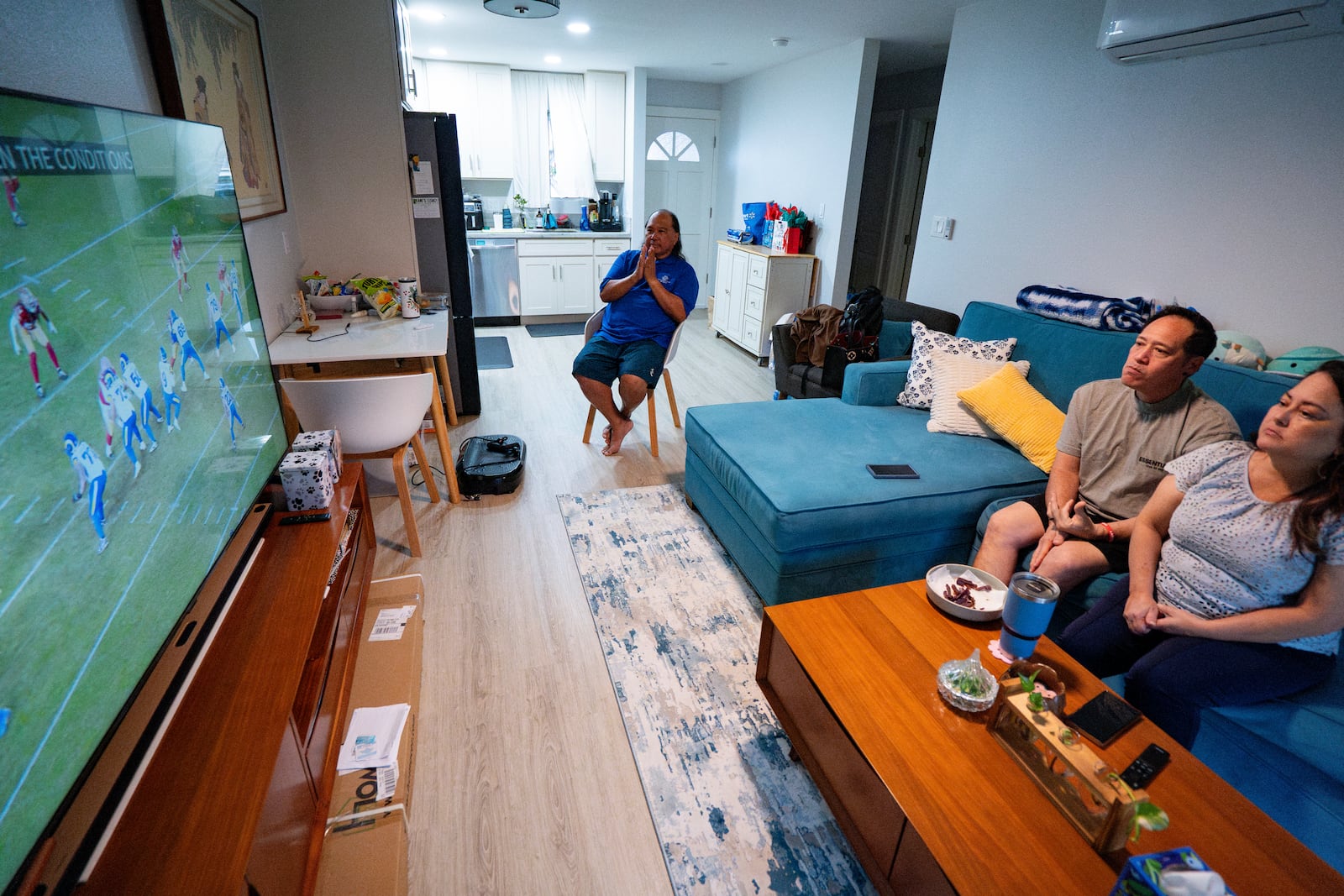 From left to right, Ron Sambrano, Tamara, and Kawehi Akiona watch football at their home, Thursday, Dec. 12, 2024, in Wailuku, Hawaii. (AP Photo/Mengshin Lin)