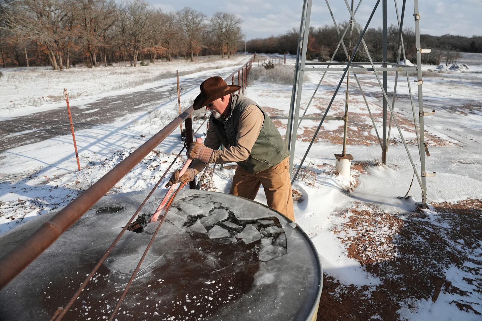 Walt Traywick uses an axe to break up frozen water in a stock tank while working on his farm Wednesday, Feb. 19, 2025, in Luther, Okla. (AP Photo/Joshua A. Bickel)