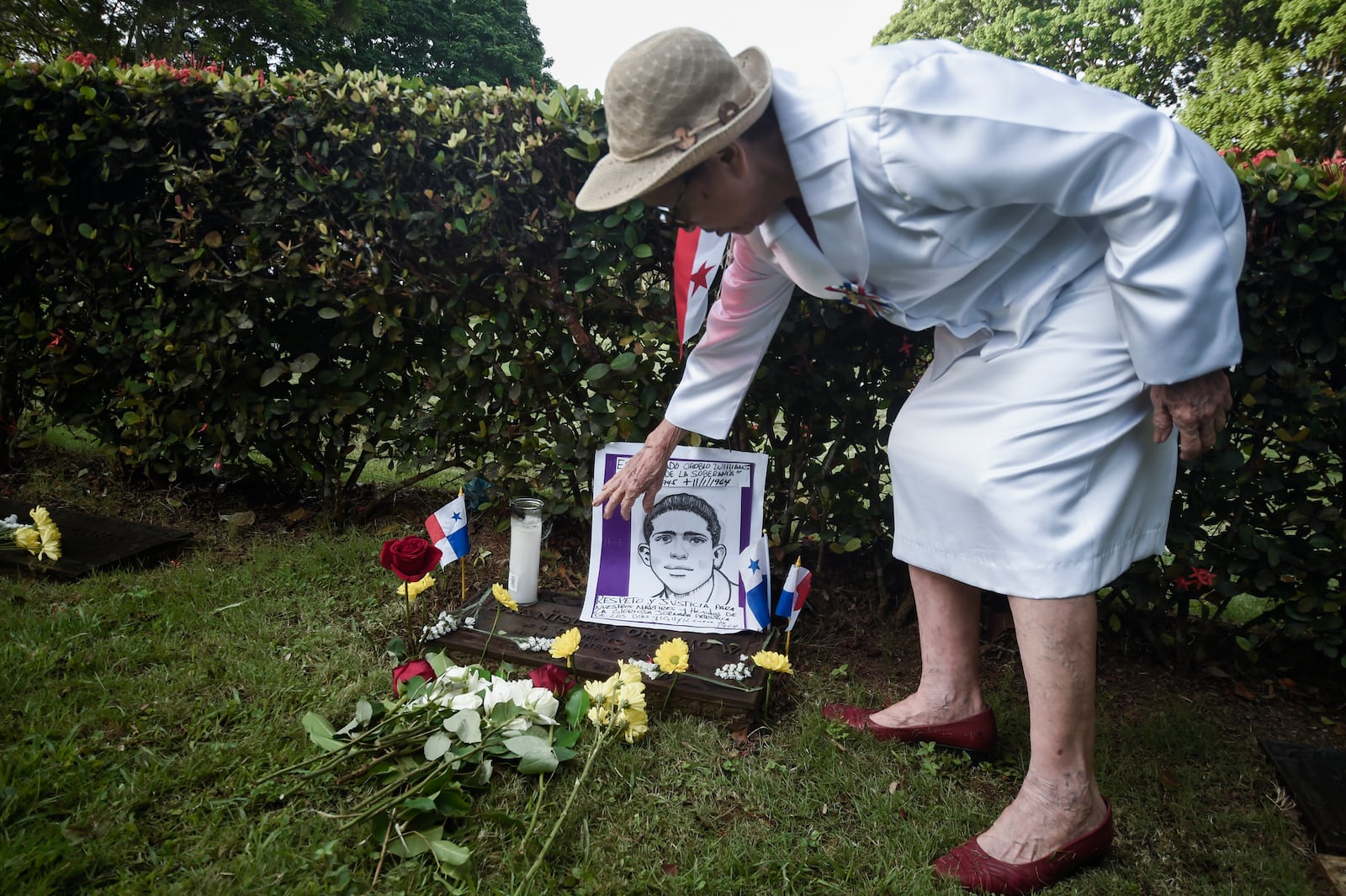 A woman places flowers by a portrait depicting one of the Panamanian students who was killed in 1964 on Martyrs Day in Panama City, Wednesday, Jan. 9, 2025. (AP Photo/Agustin Herrera)