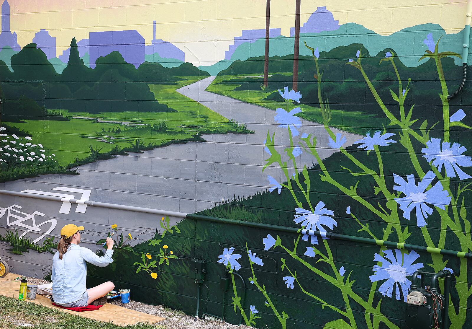 Artist Kelley Booze works on the Project Jericho mural in 2021 that welcomes bike riders to Springfield as they travel north along the bike path near the intersection of Leffel Lane and South Yellow Springs Street. BILL LACKEY/STAFF