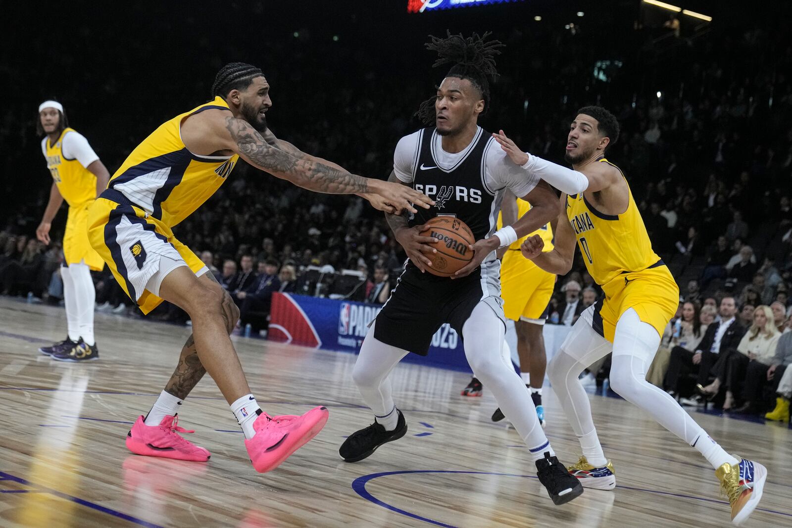 San Antonio Spurs guard Stephon Castle, center, is defended by Indiana Pacers forward Obi Toppin, left, and guard Tyrese Haliburton (0) during the second half of a Paris Games 2025 NBA basketball game in Paris, Saturday, Jan. 25, 2025. (AP Photo/Thibault Camus)