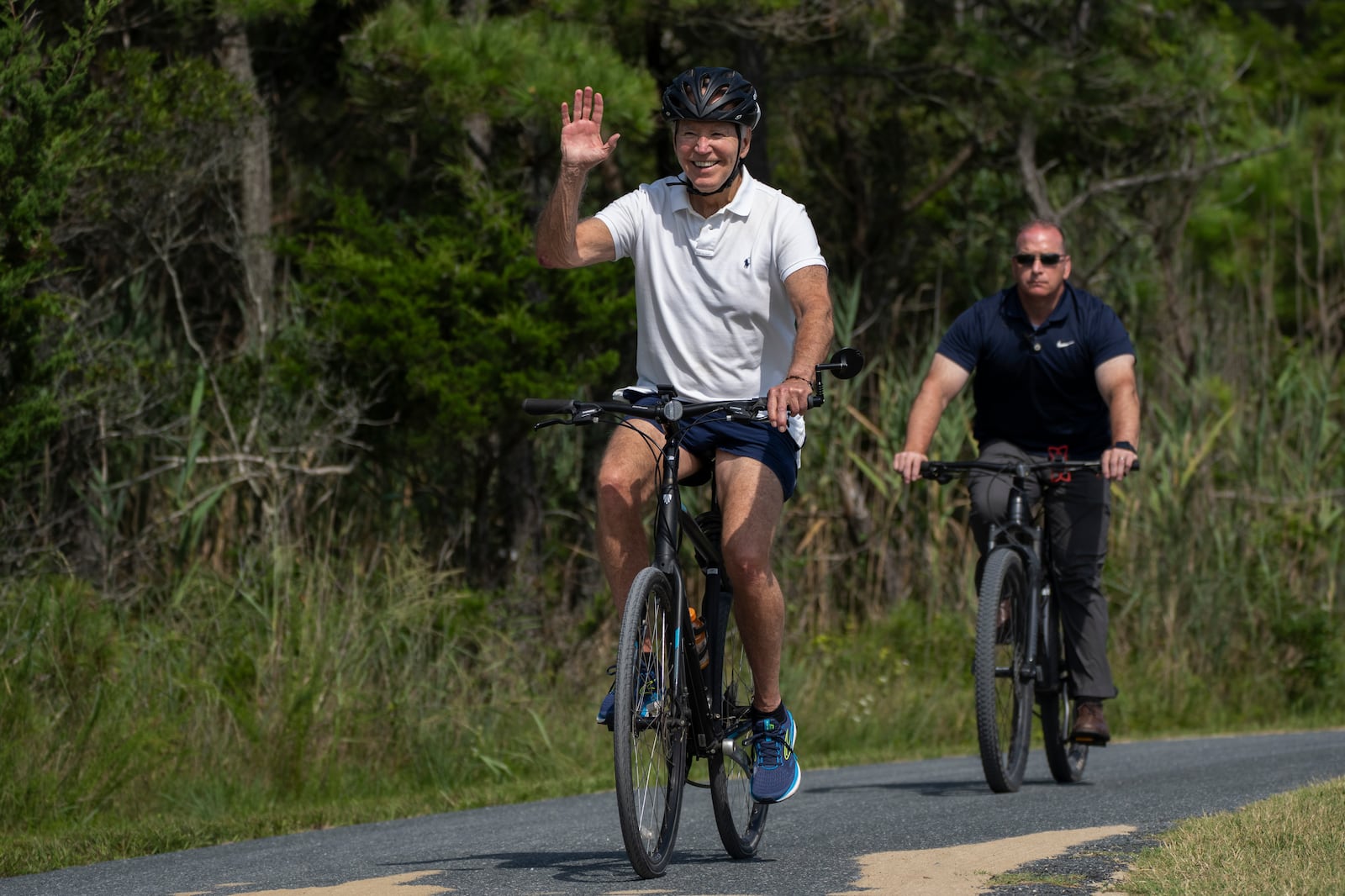 FILE - President Joe Biden waves to a cheering crowd as he rides his bike followed by a Secret Service agent at Gordons Pond in Rehoboth Beach, Del., Sunday, Aug. 11, 2024. (AP Photo/Manuel Balce Ceneta, File)