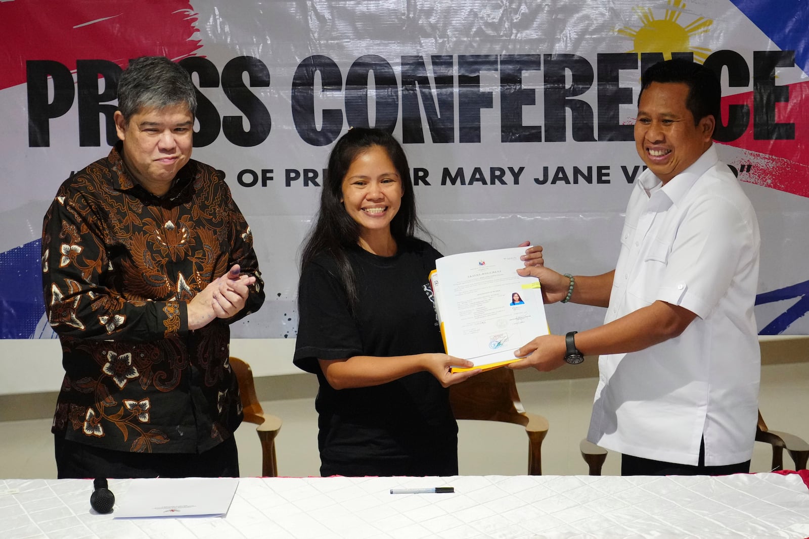 Mary Jane Veloso, center, a Filipina who was on death row in Indonesia and was nearly executed by firing squad in 2015, receives her transfer document from acting Deputy Coordinating Minister for Immigration and Correctional Affairs I Nyoman Gede Surya Mataram as Philippine's Undersecretary for Migration Affairs at the Department of Foreign Affairs Eduardo Jose de Vega, left, applauds during a handover ceremony prior to her repatriation to the Philippines, at Soekarno-Hatta International Airport in Tangerang, Indonesia, Tuesday, Dec. 17, 2024. (AP Photo/Tatan Syuflana)