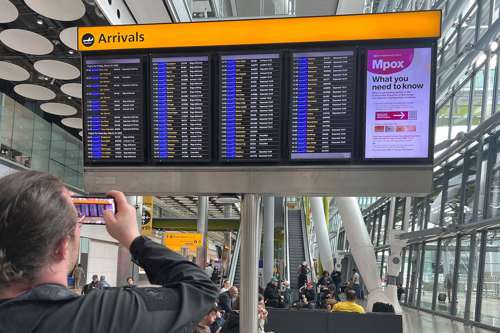 A man takes a photo of the flight information display in the arrivals hall at Heathrow Terminal 5 in London, Saturday March 22, 2025, after flights resumed at the airport. (Maja Smiejkowska/PA via AP)