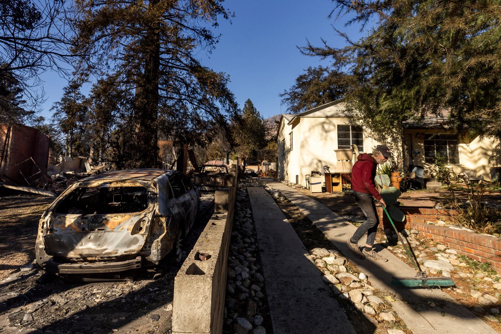 David Slater, right, clears the driveway from his home, spared from the Eaton Fire, Jan. 12, 2025, in Altadena, Calif. (AP Photo/Ethan Swope)