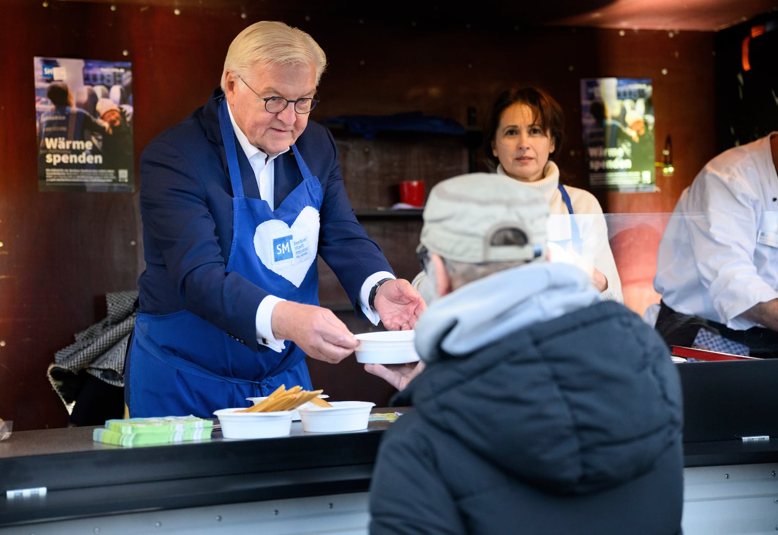 German President Frank-Walter Steinmeier, left, hands out soup to people in need in front of Berlin Central Station during a visit to mark the 30th anniversary of the Berlin City Mission's cold buses. (Bernd von Jutrczenka/dpa via AP)