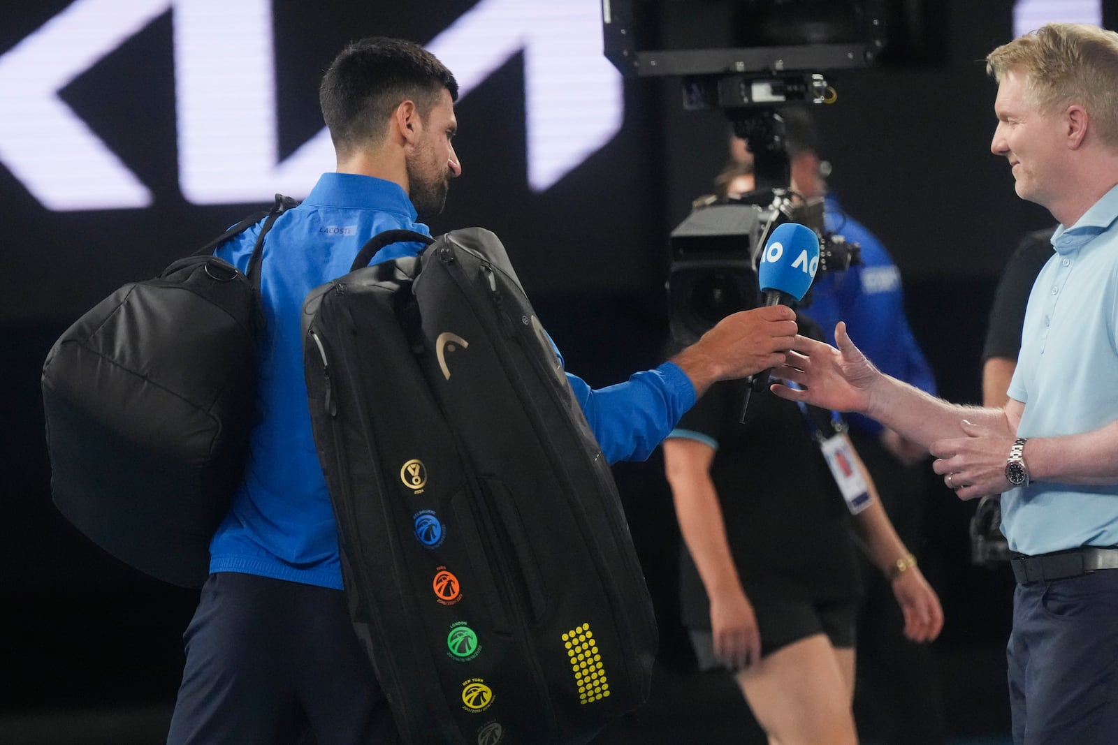 Novak Djokovic of Serbia hands a microphone to Jim Courier after his match against Jiri Lehecka of the Czech Republic during their fourth round match at the Australian Open tennis championship in Melbourne, Australia, Sunday, Jan. 19, 2025. (AP Photo/Mark Baker)