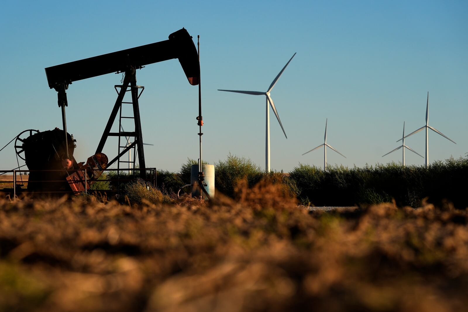 FILE - Pumpjacks operate in the foreground as the Buckeye Wind Energy wind farm rises in the distance, Sept. 30, 2024, near Hays, Kan. (AP Photo/Charlie Riedel, File)