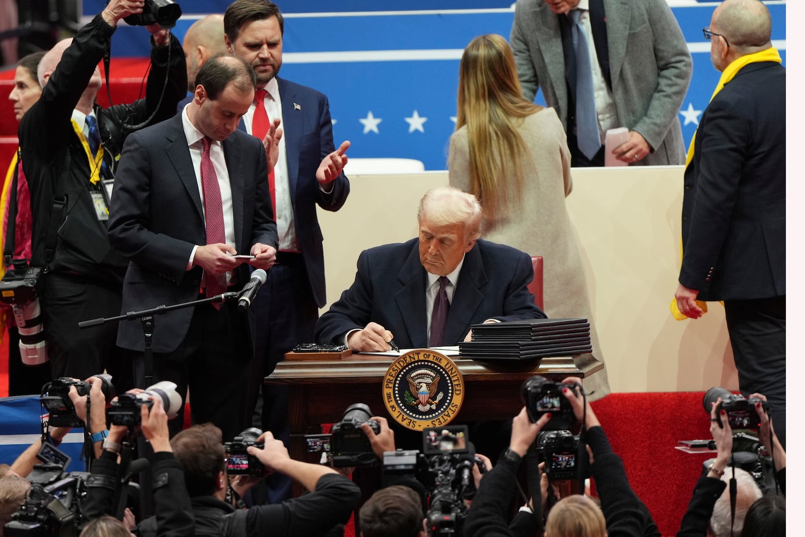 President Donald Trump signs an executive order as Vice President JD Vance watches at an indoor Presidential Inauguration parade event in Washington, Monday, Jan. 20, 2025. (AP Photo/Matt Rourke)