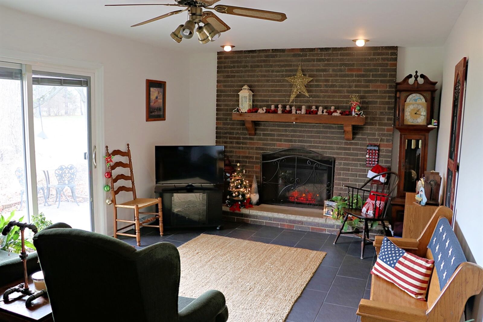 The family room has a brick fireplace. Eyeball lighting accents the fireplace with raised hearth and wood-beam mantel. 