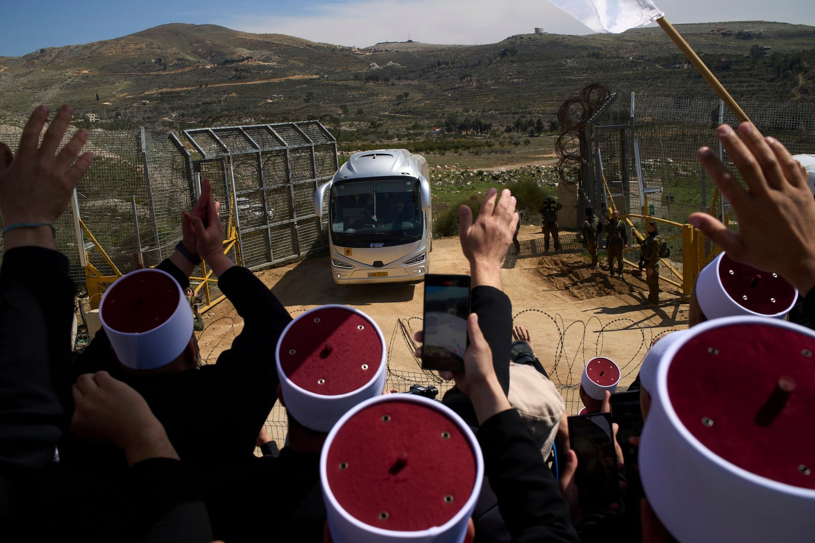 Buses carrying members of the Syrian Druze community are welcomed by Druze clerics at the border with Syria, as they enter into the village of Majdal Shams, in the Israeli-controlled Golan Heights, Friday, March 14, 2025. (AP Photo/Leo Correa)