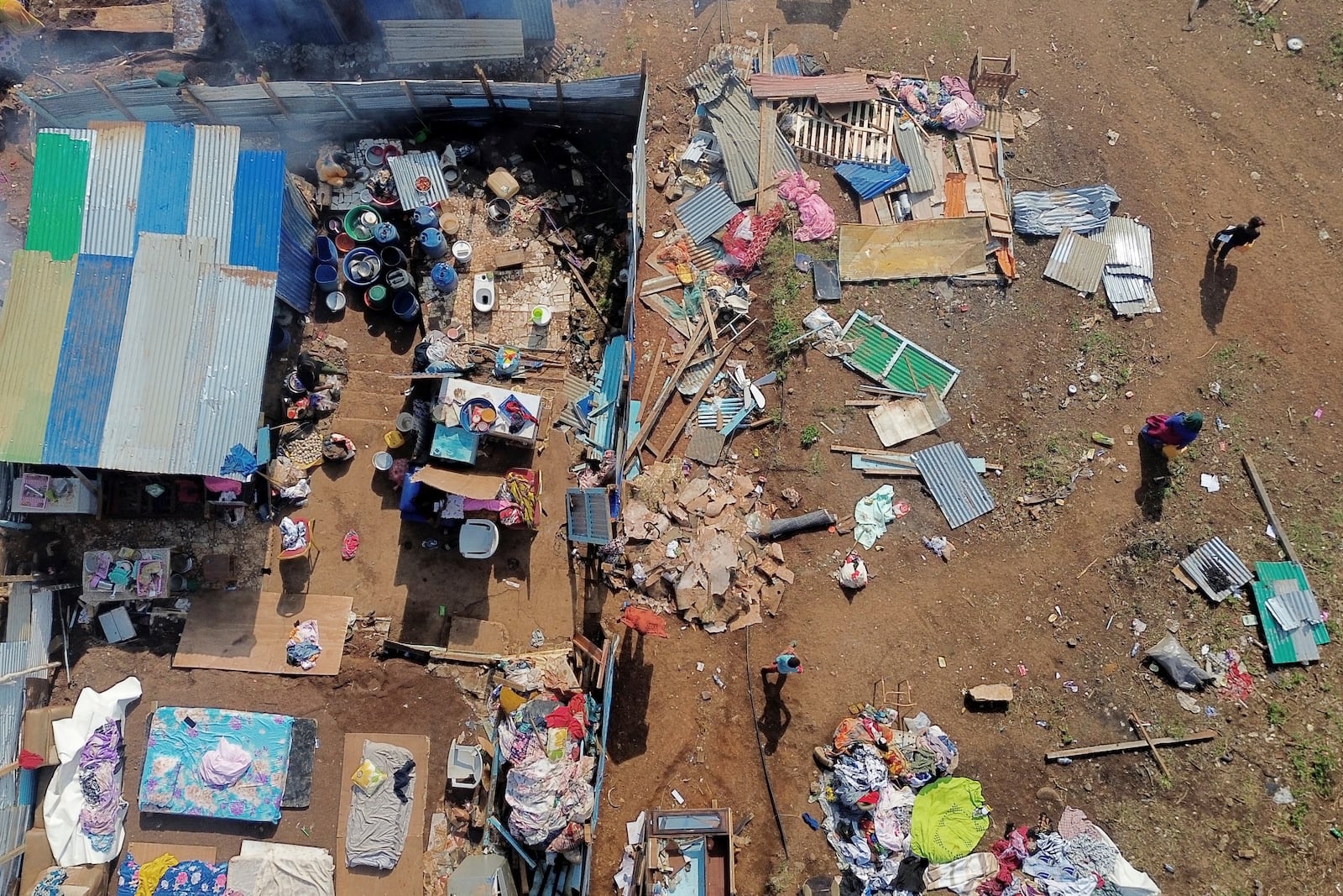 People walk by destroyed homes in the Barakani, Mayotte, informal settlement, Saturday, Dec. 21, 2024. (AP Photo/Adrienne Surprenant)