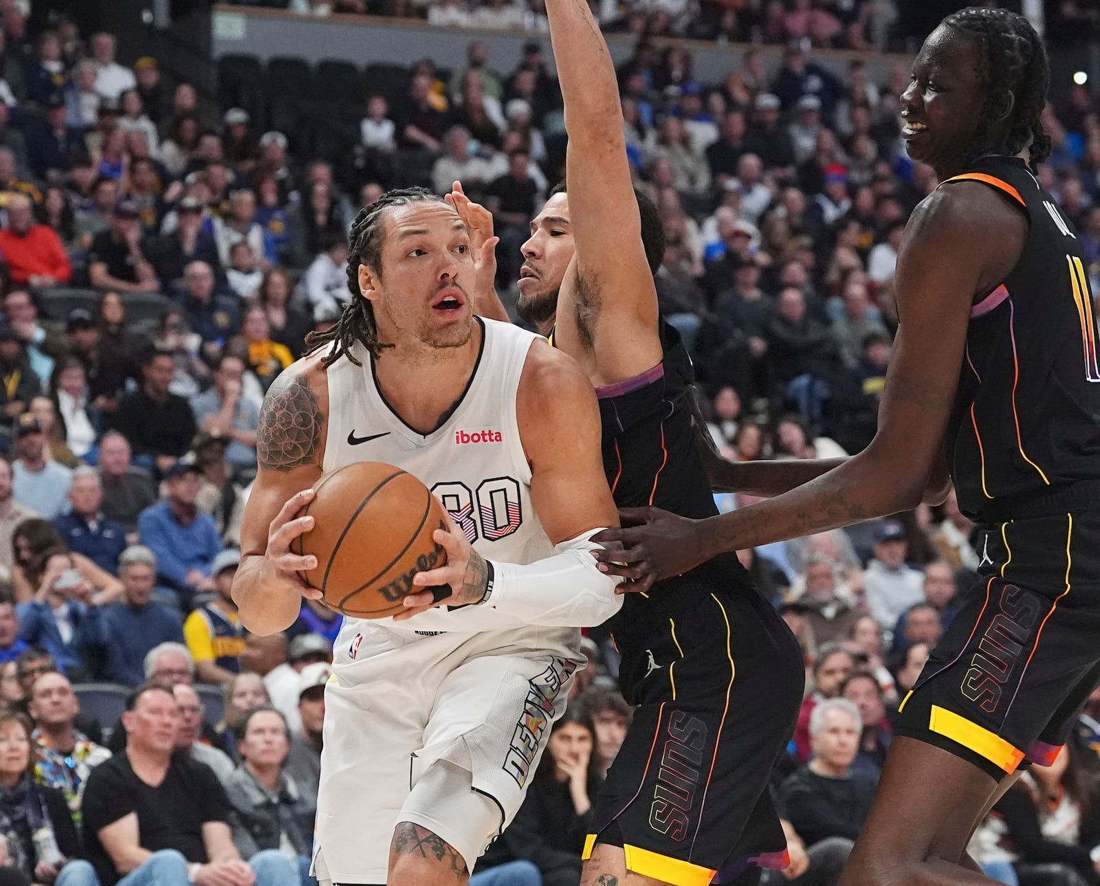 Denver Nuggets forward Aaron Gordon, left, drives past Phoenix Suns guard Devin Booker, center, and center Bol Bol, right, in the first half of an NBA basketball game Friday, March 7, 2025, in Denver. (AP Photo/David Zalubowski)