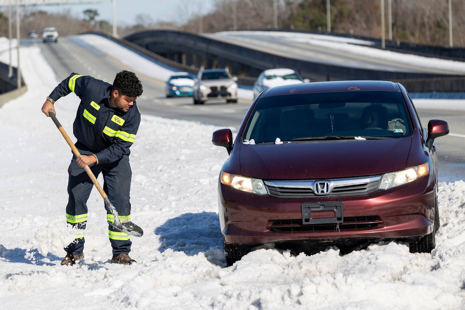 An employee with Elite Towing who goes by the name of "Grasshopper Junior" shovels out a car stuck on I-526 after a winter storm dropped ice and snow Wednesday, Jan. 22, 2025, on North Charleston, S.C. (AP Photo/Mic Smith)