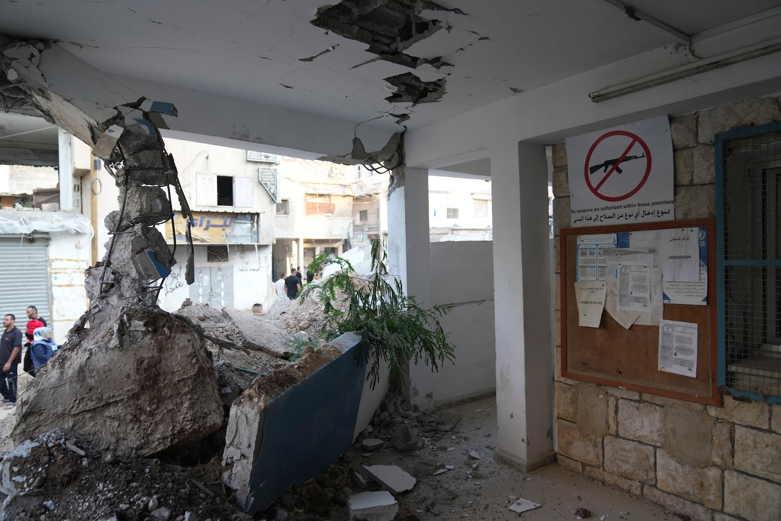 Palestinians pass by the rubble of the United Nations Office for helping Palestinian refugees, UNRWA, that was partly demolished during the Israeli army operation in the West Bank refugee camp of Nur Shams, in Tulkarem Thursday, Oct. 31, 2024. (AP Photo/Nasser Nasser)