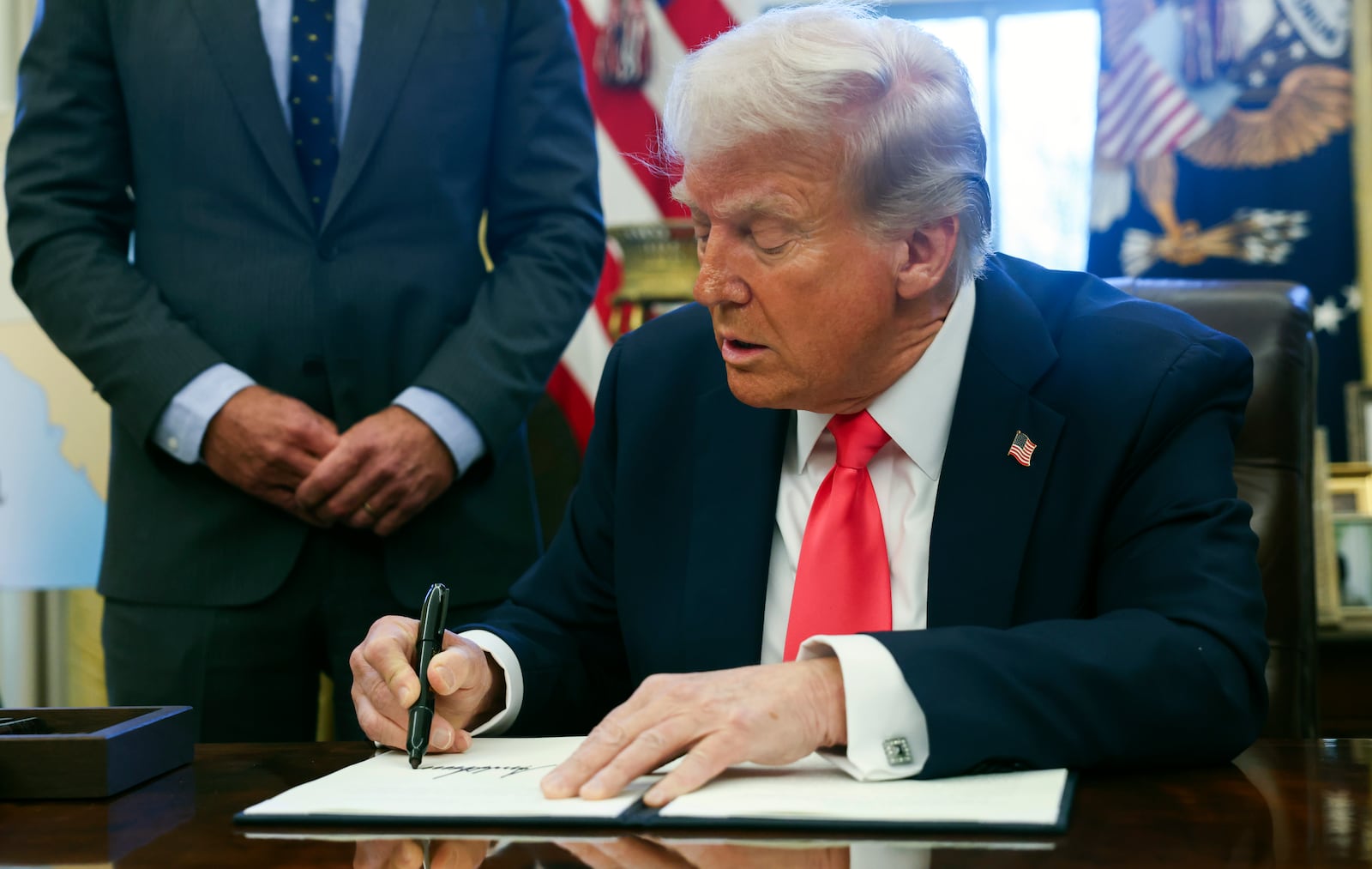 President Donald Trump signs an executive order in the Oval Office at the White House in Washington, Thursday, Feb. 25, 2025. (Pool via AP)