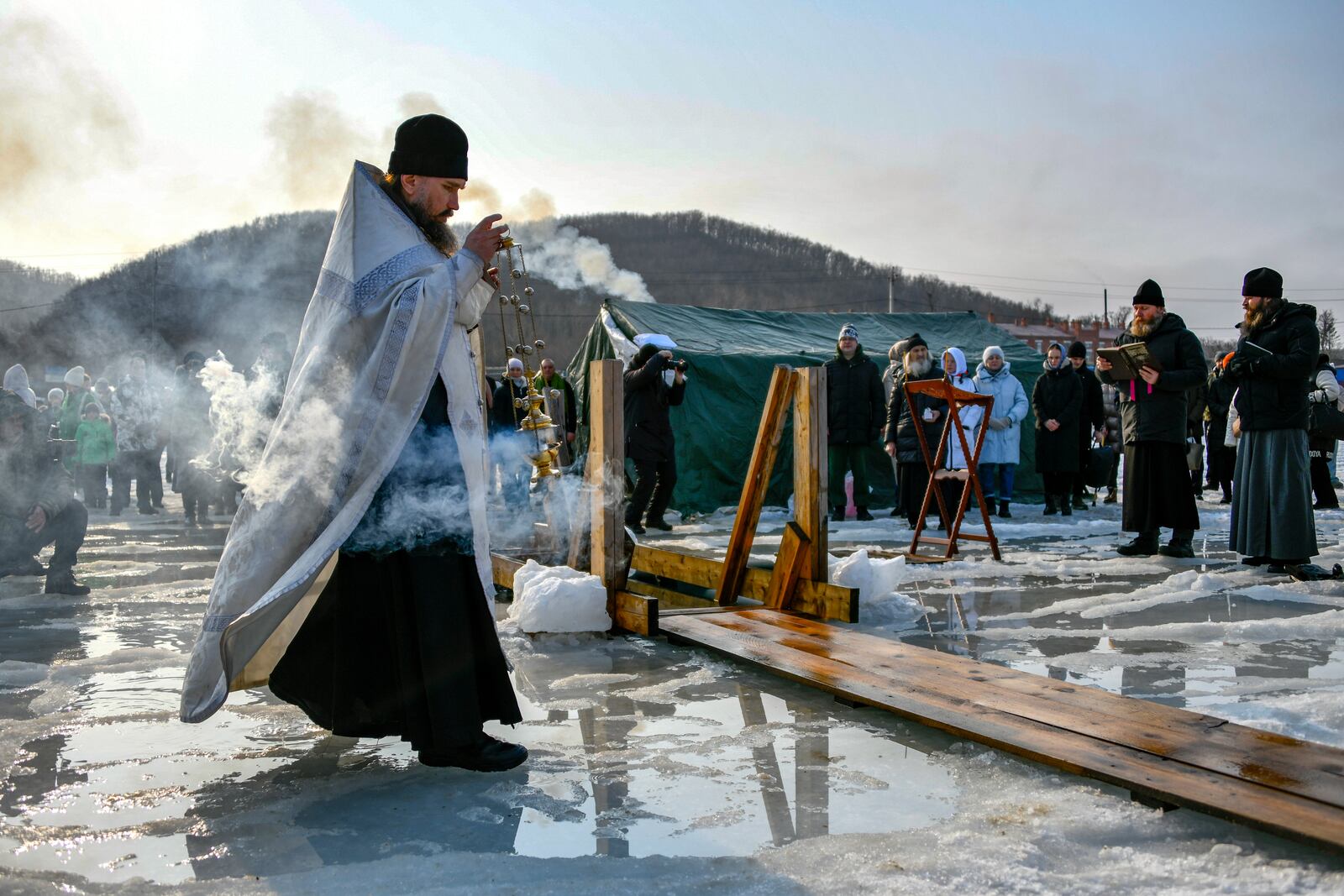 A priest makes a religion service while blessing the icy water before celebrating the Orthodox Epiphany near the St. Serafimovsky Monastery on Russian Island in Russian far east port Vladivostok, Russia, Sunday, Jan. 19, 2025.