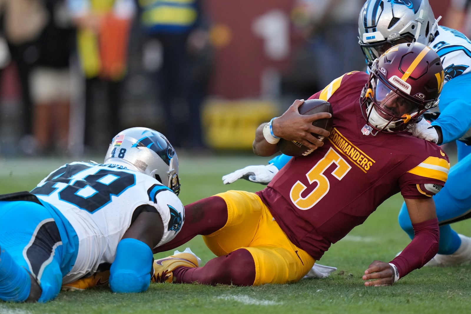 Washington Commanders quarterback Jayden Daniels (5) is tackled by Carolina Panthers linebacker Thomas Incoom (48) during the first half of an NFL football game, Sunday, Oct. 20, 2024, in Landover, Md. (AP Photo/Stephanie Scarbrough)