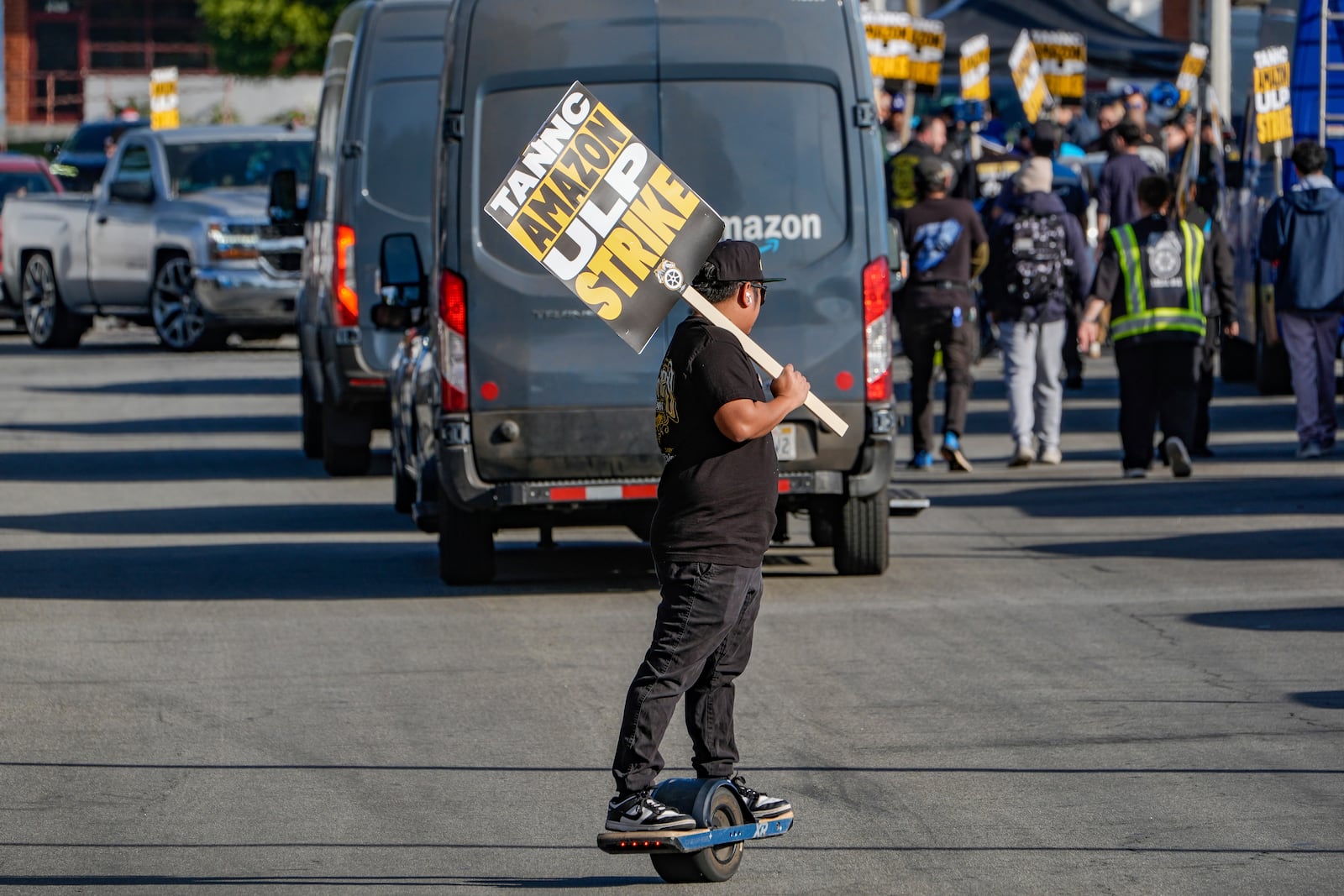 UPS driver Jhon Solidum, a member of the Teamsters union, rides a one wheeler to support the Amazon workers striking outside an Amazon Fulfillment Center as Teamsters seek labor contract nationwide, Thursday, Dec. 19, 2024, in City of Industry, Calif. (AP Photo/Damian Dovarganes)