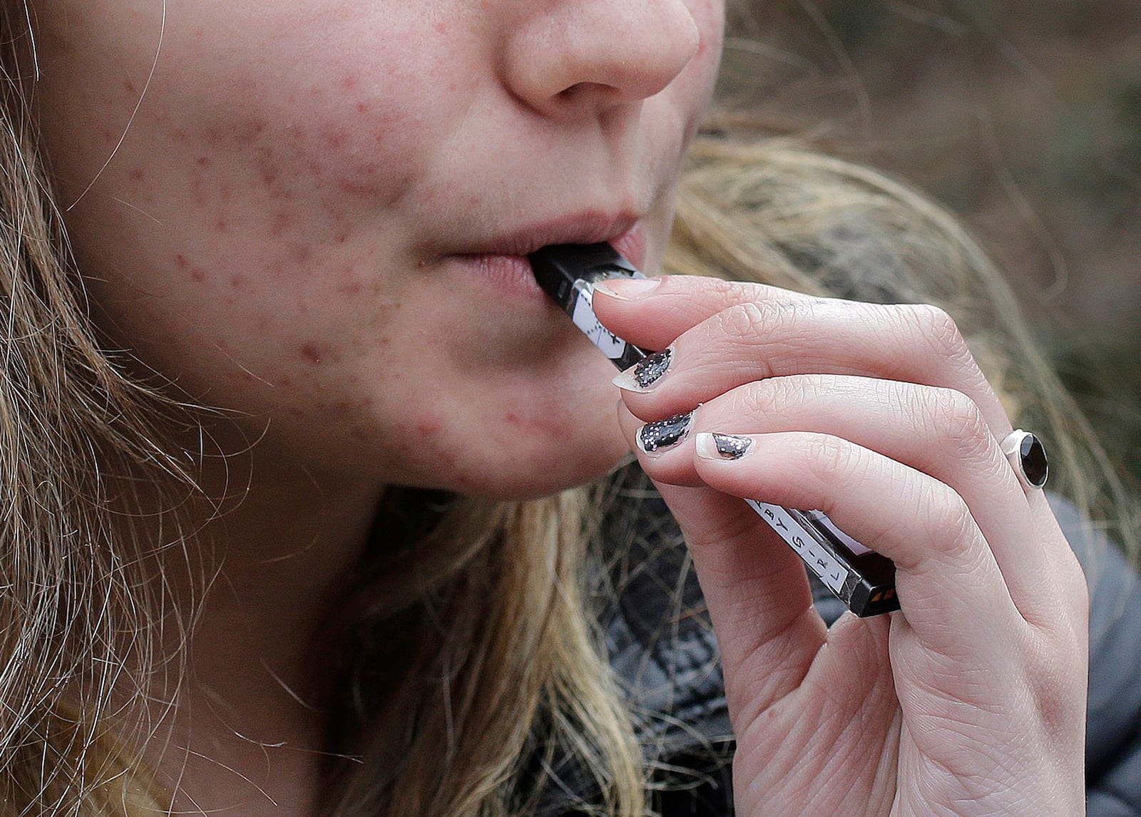 FILE - A high school student uses a vaping device near a school campus in Cambridge, Mass., April 11, 2018. (AP Photo/Steven Senne, File)