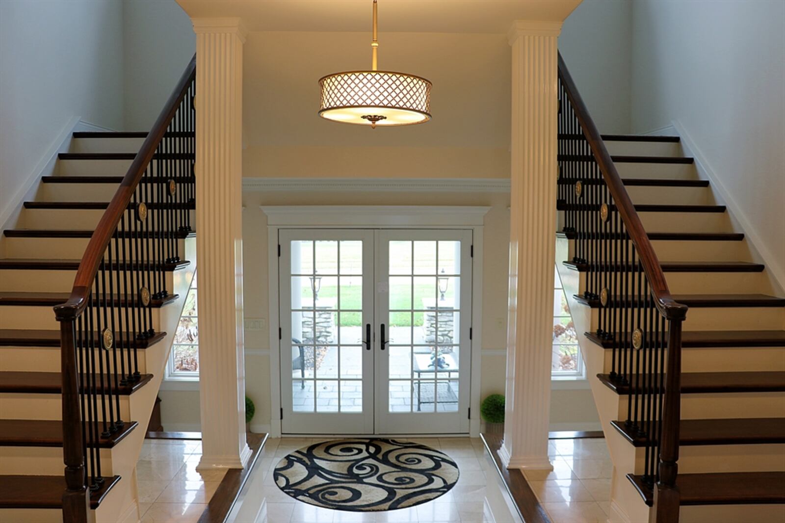 Double glass doors open into a grand foyer with polished ceramic-tile flooring and dark wood trim. Fluted columns accent the three-step entry to the main living space, and ceramic-tile display nooks are nestled under the split staircase.