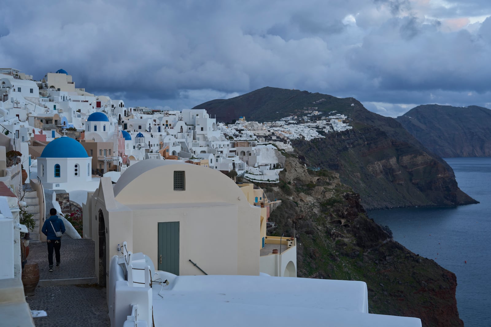 A tourist approaches blue-domed Orthodox churches in the town of Oia on the earthquake-struck island of Santorini, Greece, Tuesday, Feb. 4, 2025. (AP Photo/Petros Giannakouris)