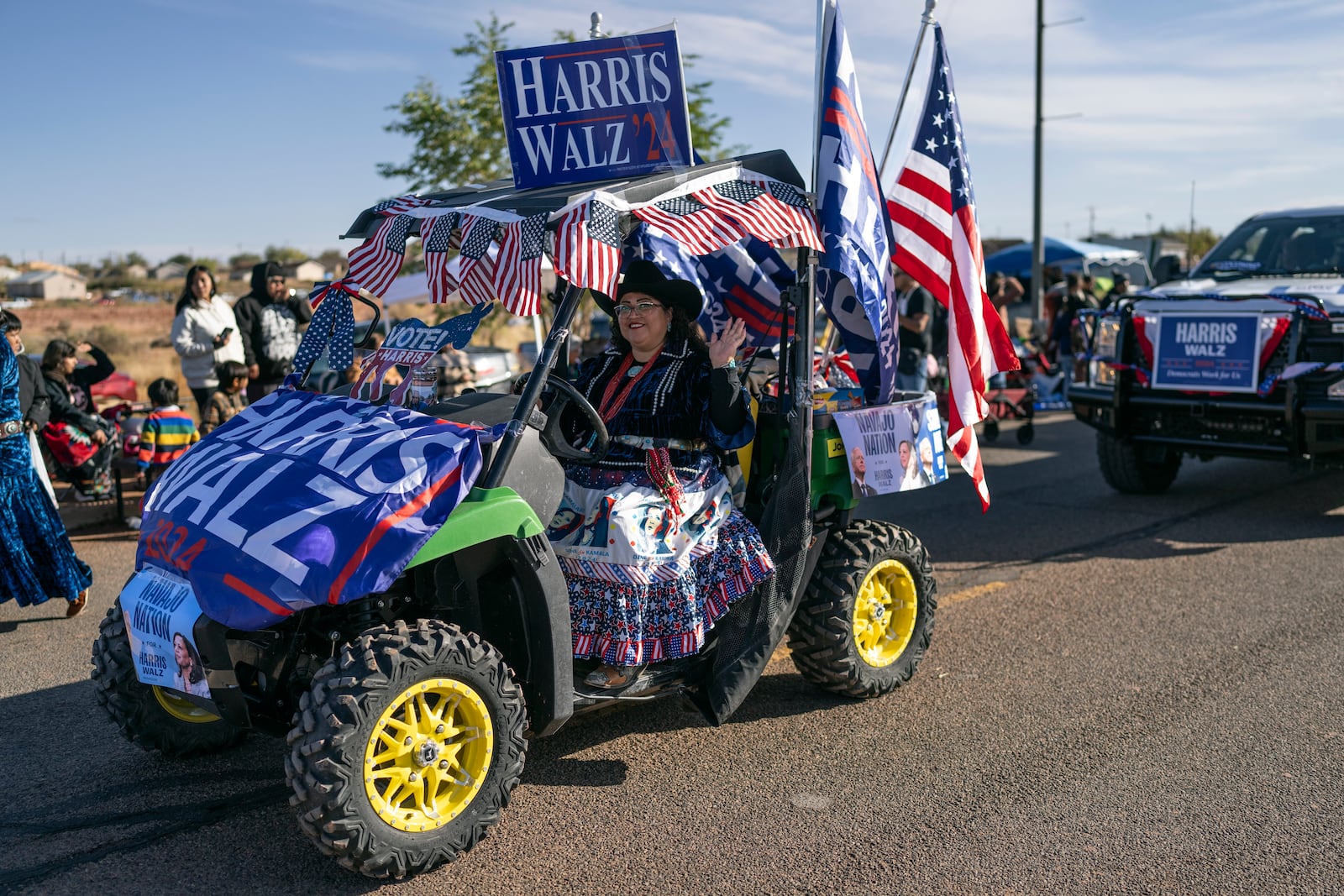 A Navajo woman waves as she campaigns for presidential hopeful Kamala Harris in a caravan of Democratic-themed floats, at the Western Navajo Fair in Tuba City, Ariz., Saturday, Oct. 19, 2024. Natives, which make up 5.2% of the state’s population, voted in big numbers for the Democratic party in 2020 and were credited with swinging the state blue for the first time in decades. (AP Photo/Rodrigo Abd)