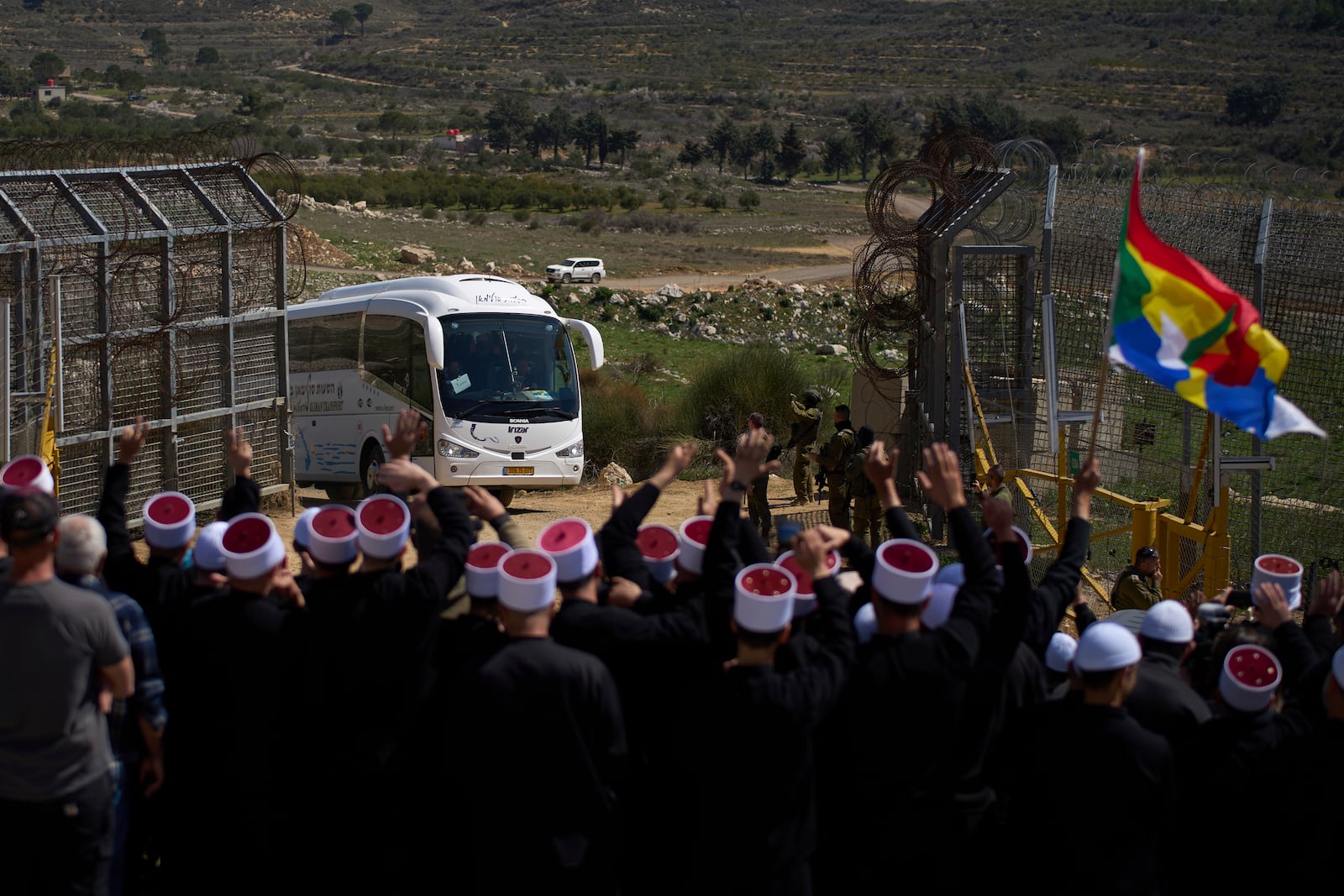 Buses carrying members of the Syrian Druze community are welcomed by Druze clerics at the border with Syria, as seen from the village of Majdal Shams, in the Israeli-controlled Golan Heights, Friday, March 14, 2025. (AP Photo/Leo Correa)