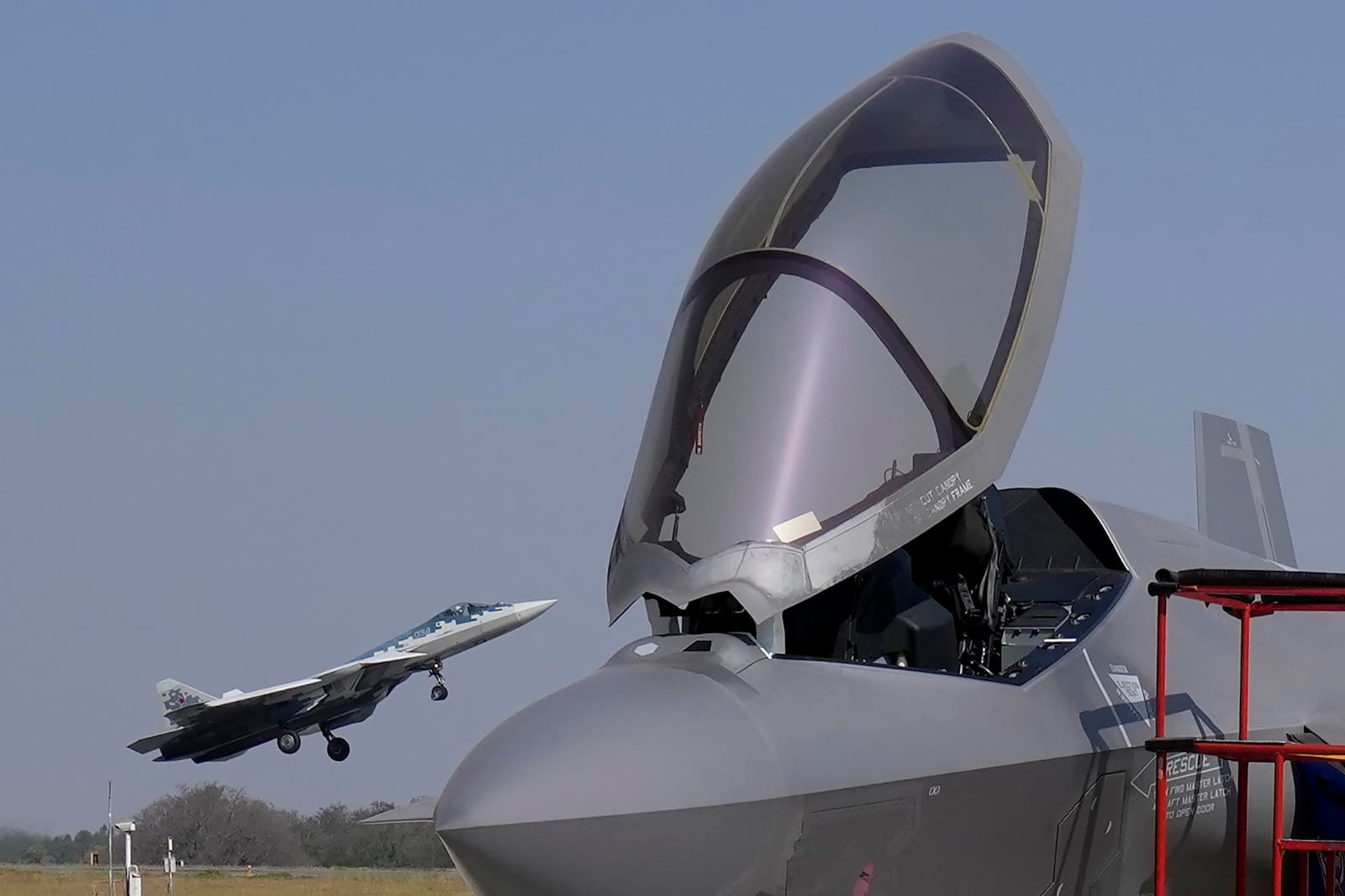 Russia's Su-57 fighter aircraft takes off behind the U.S. Air Force fighter aircraft F-35, parked at the static display area, on the last day of the Aero India 2025, a biennial event, at Yelahanka air base in Bengaluru, India, Friday, Feb. 14, 2025. (AP Photo/Aijaz Rahi)