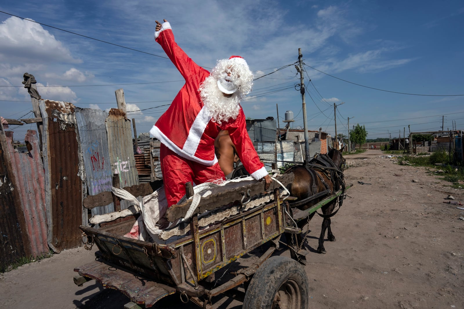 FILE - Tito Perez, dressed as Santa Claus, waves to children while standing on the back of a horse cart, at a pre-Christmas celebration organized by "Los Chicos de la Via" soup kitchen, in Buenos Aires, Argentina, Saturday, Dec. 23, 2023. (AP Photo/Rodrigo Abd, File)