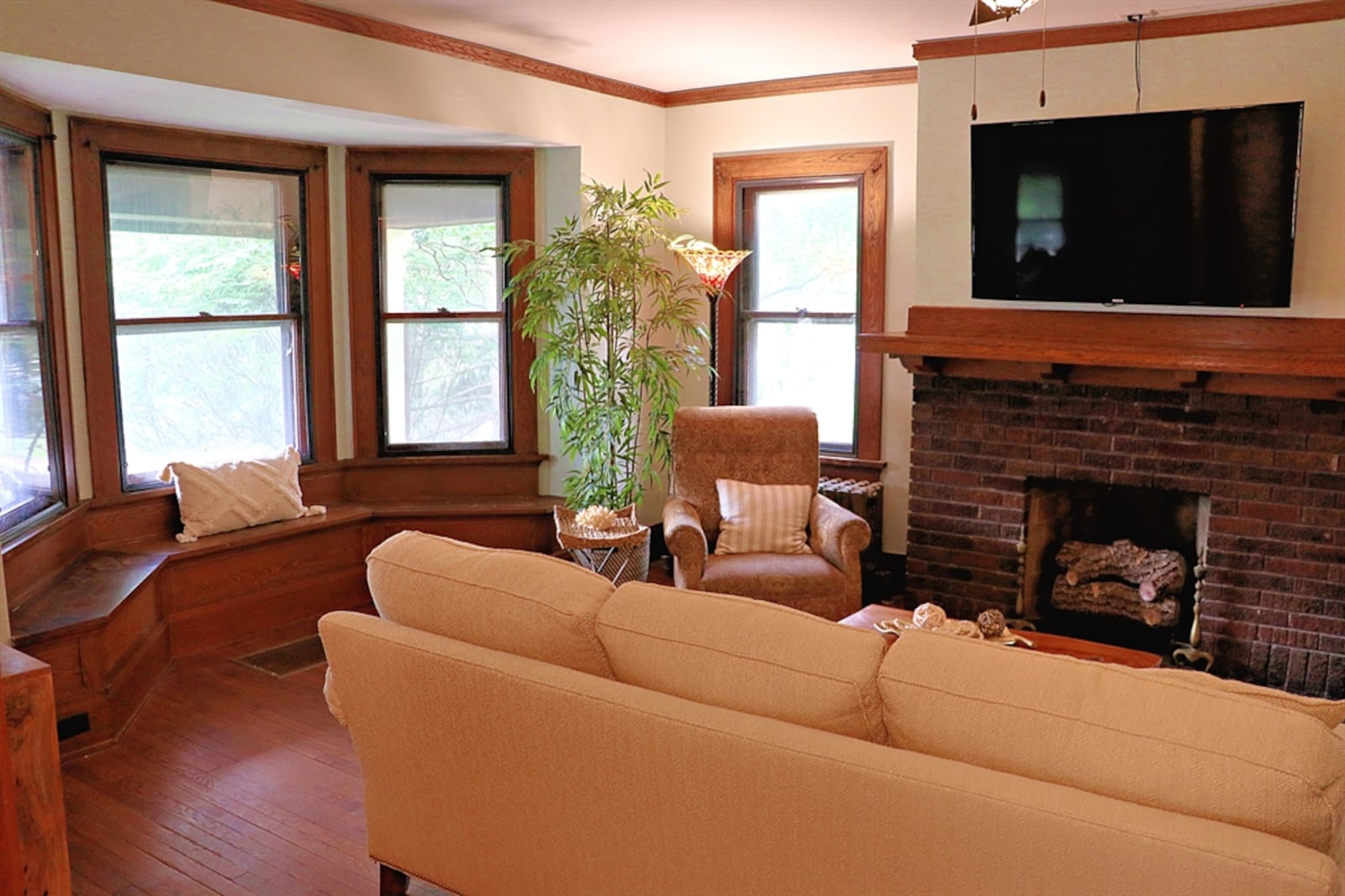 The living room features a bay bump-out with a built-in window seat. The decorative fireplace has a brick surround and wood mantel. 