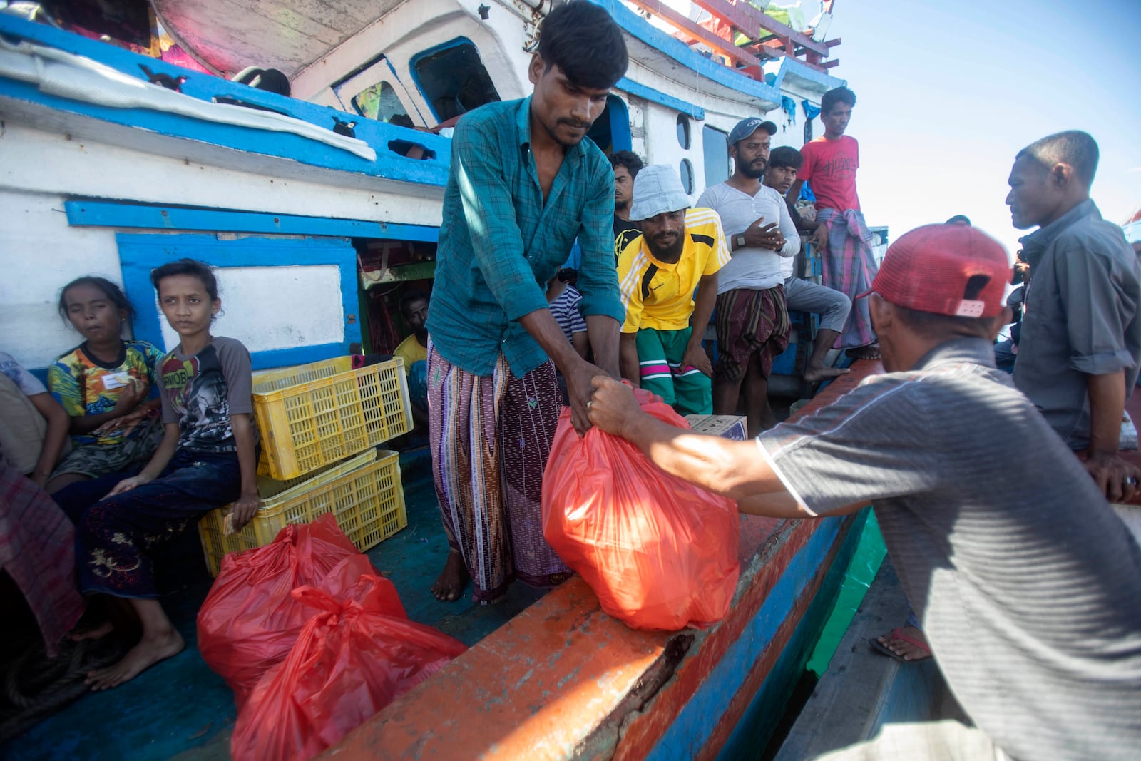 A Rohingya man receives food delivered by local fishermen to their boat anchored in the waters near the coast of Labuhan Haji, Aceh province, Indonesia, Tuesday, Oct. 22, 2024. (AP Photo/Binsar Bakkara)