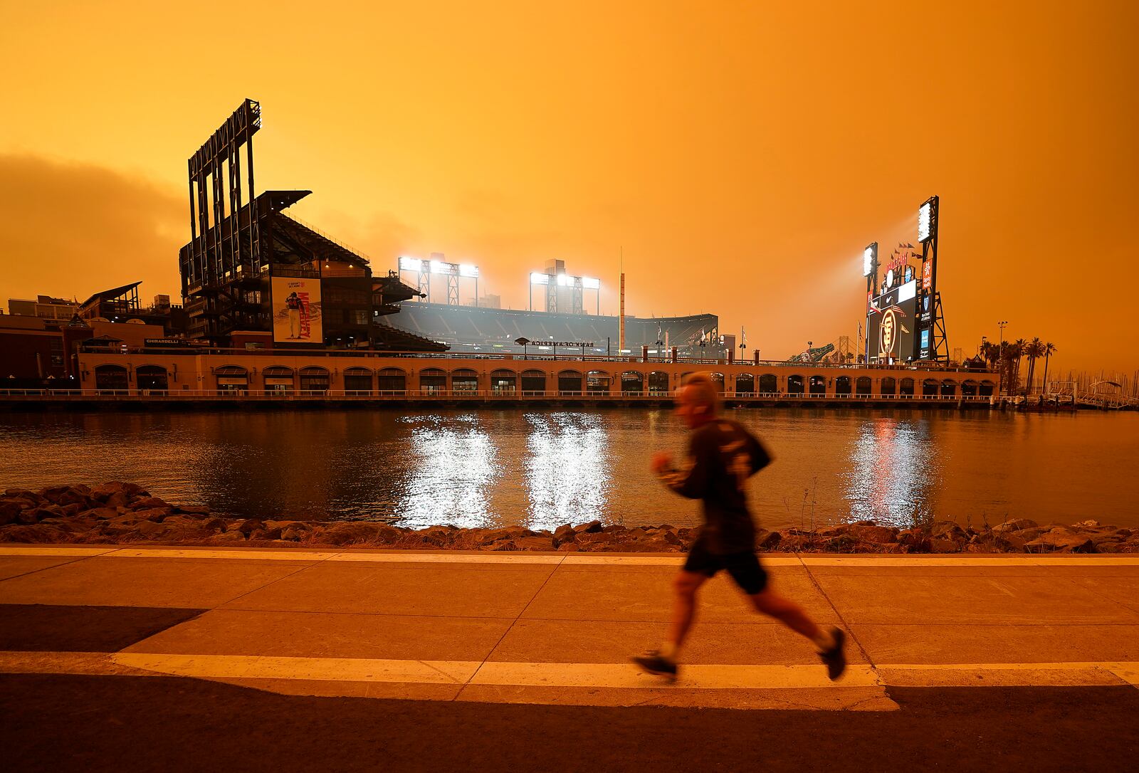 Under darkened skies from wildfire smoke, a jogger makes his way along McCovey Cove outside Oracle Park on Wednesday, Sept. 9, 2020, in San Francisco. People from San Francisco to Seattle woke Wednesday to hazy clouds of smoke lingering in the air, darkening the sky to an eerie orange glow that kept street lights illuminated into midday, all thanks to dozens of wildfires throughout the West. (AP Photo/Tony Avelar)