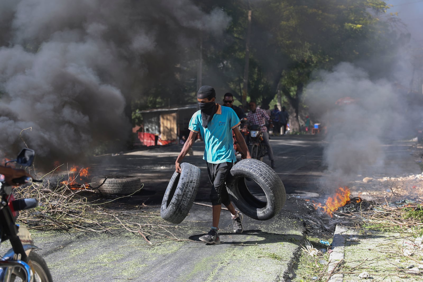 A resident carries tires to be added to a burning barricade to deter gang members from entering his neighborhood, in Port-au-Prince, Haiti, Tuesday, Nov. 19, 2024. (AP Photo/Odelyn Joseph)