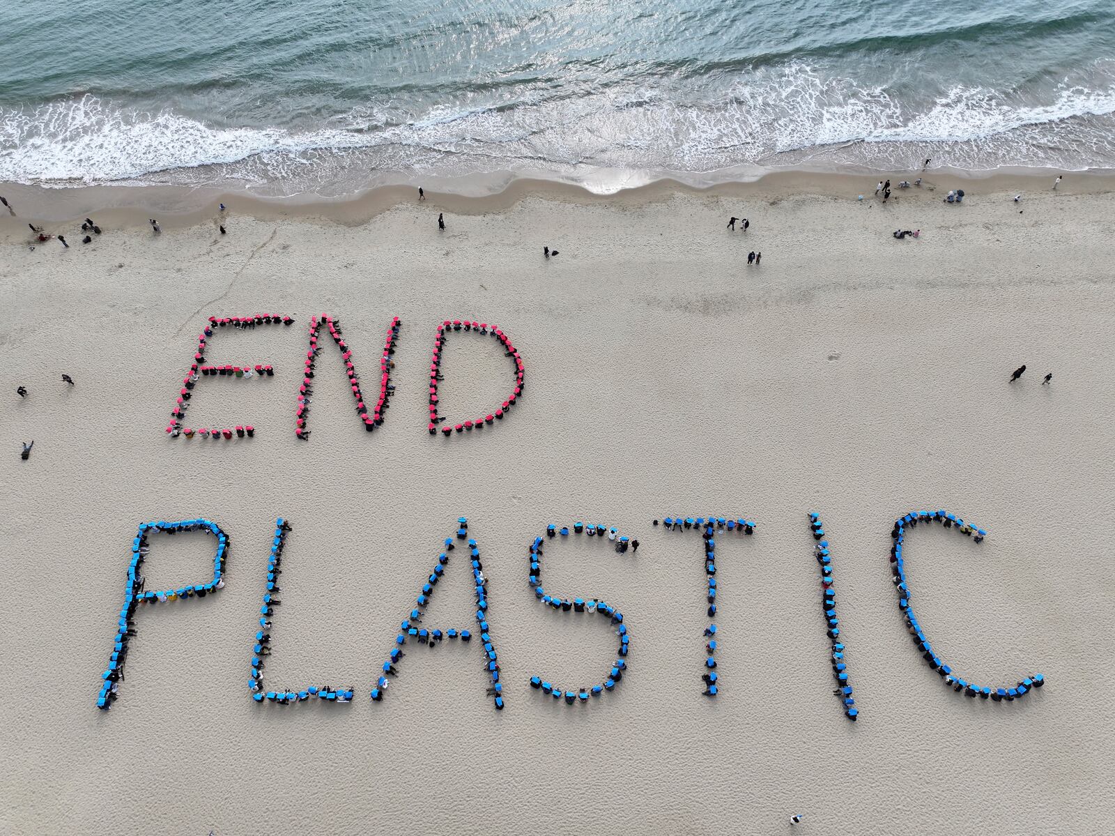 Environment activists perform a human sign calling for a strong global plastics treaty ahead of the fifth session of the Intergovernmental Negotiating Committee on Plastic Pollution which sets to be held from Nov. 25 to Dec. 1 on the beach in Busan, South Korea, Sunday, Nov. 24, 2024. (Son Hyung-joo/Yonhap via AP)