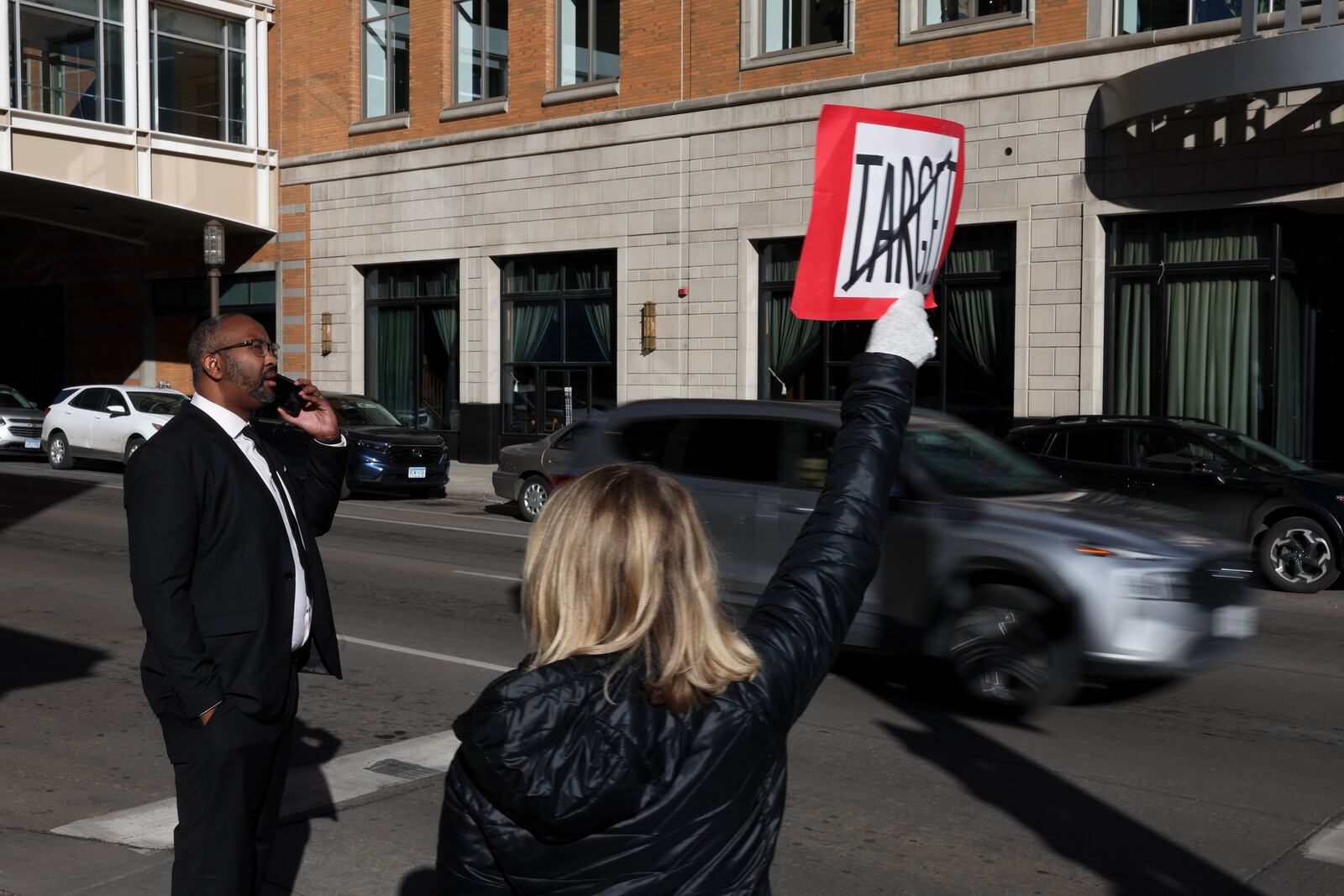 Becky Dankowski, center, of Minneapolis, holds an anti-Target sign to traffic while Jaylani Hussein, executive director of the Minnesota chapter of the Council on American-Islamic Relations, takes a phone call before a news conference outside Target Corporation's headquarters Thursday, Jan. 30, 2025, in Minneapolis, Minn. (AP Photo/Ellen Schmidt)